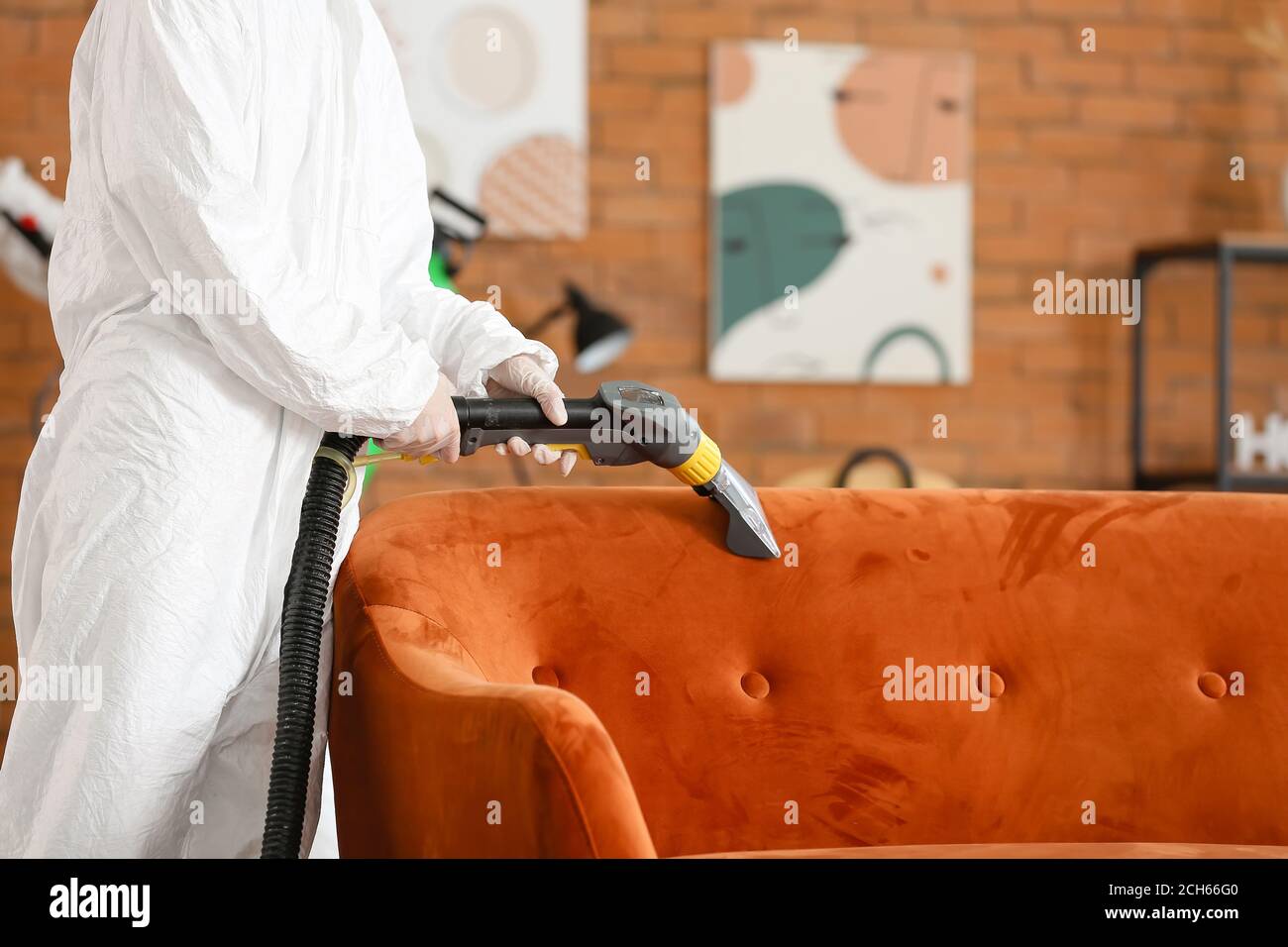 Worker in biohazard costume removing dirt from sofa in house Stock Photo