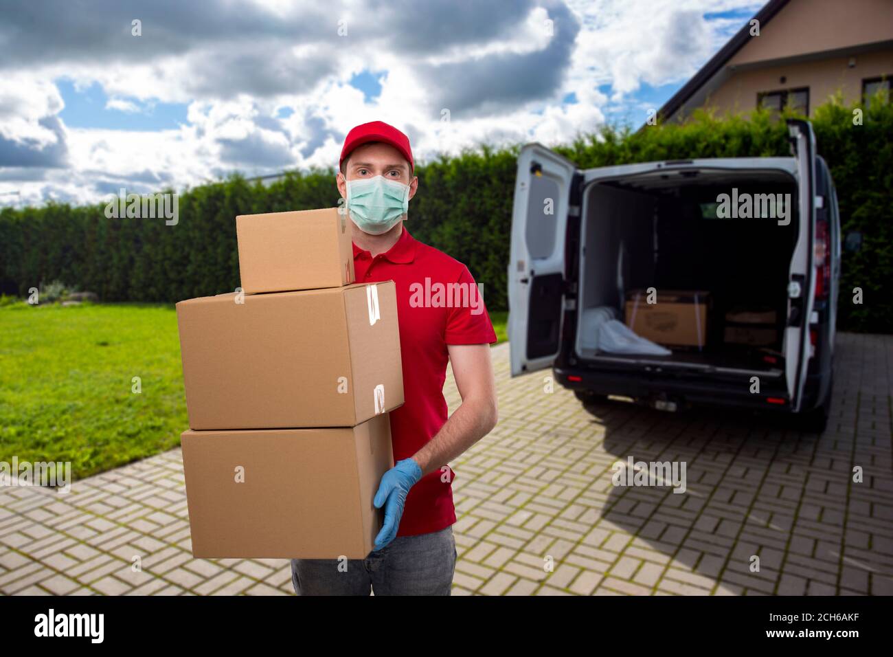 Delivery Man Wearing Medical Mask and Gloves Holding Carton Boxes. Delivery Boy with Boxes in Hands at Delivery Point Stock Photo