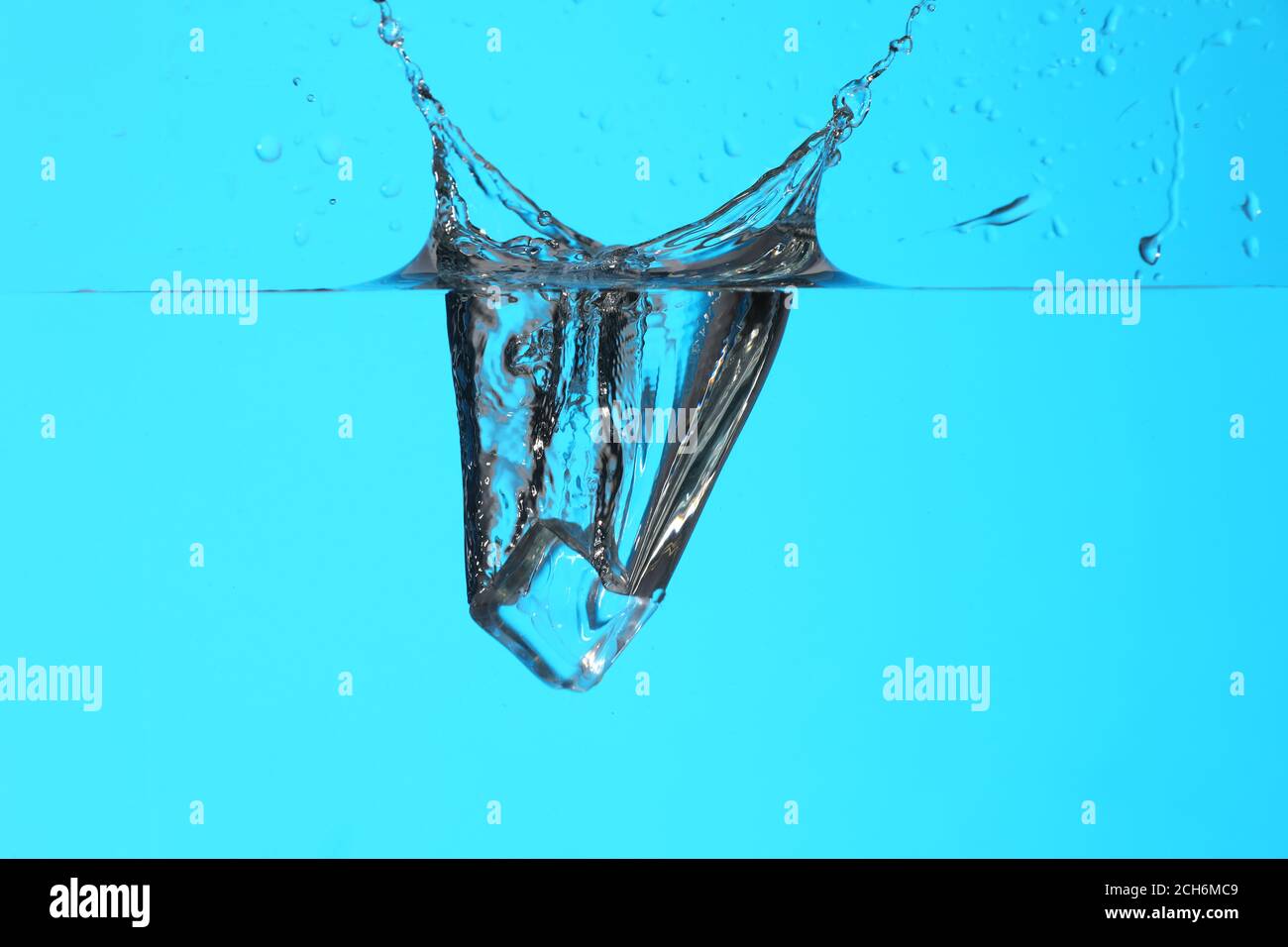 Falling of ice cube into water on color background Stock Photo - Alamy