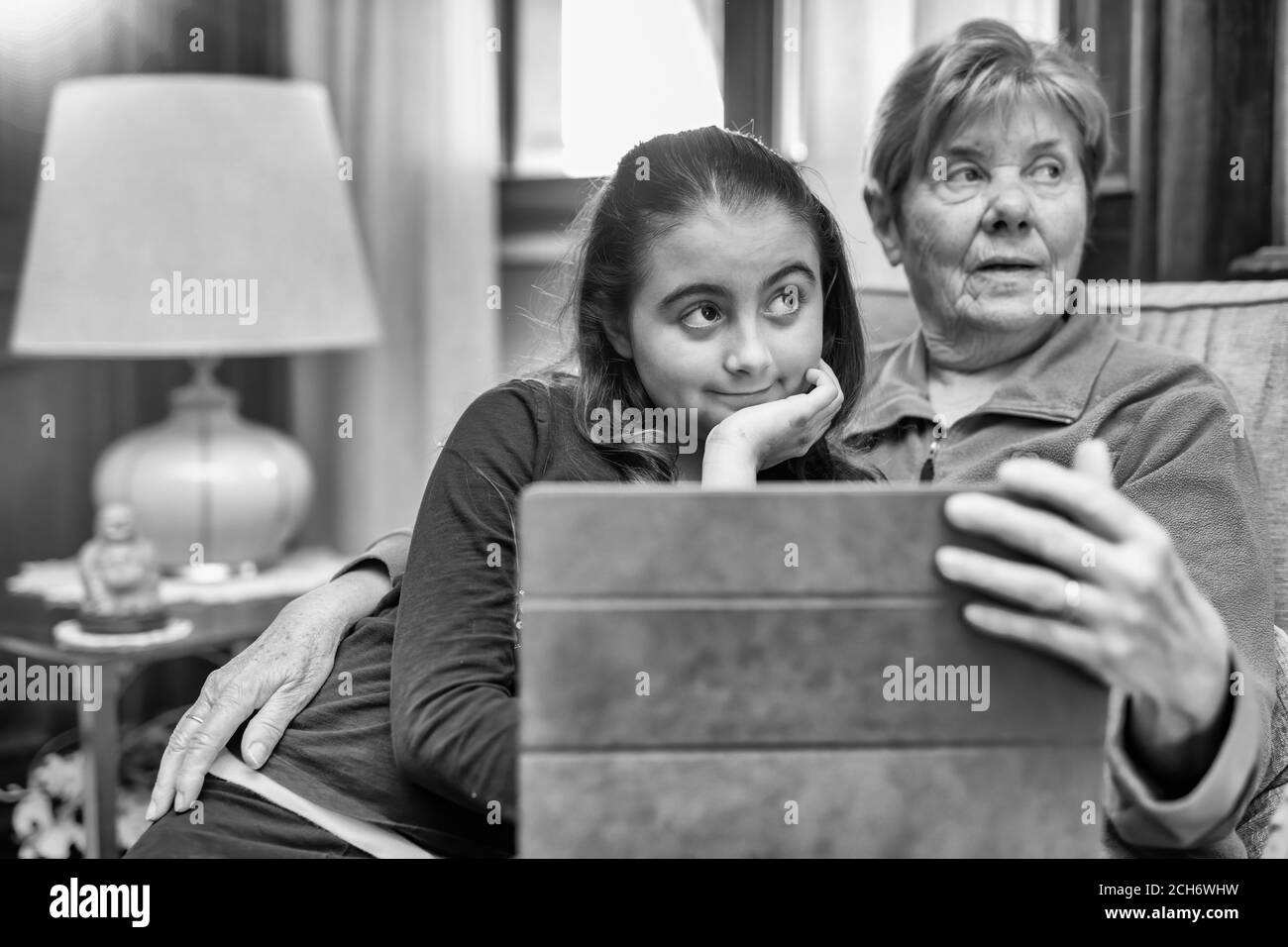 Young girl playing with tablet with her grandmother at home. Stock Photo