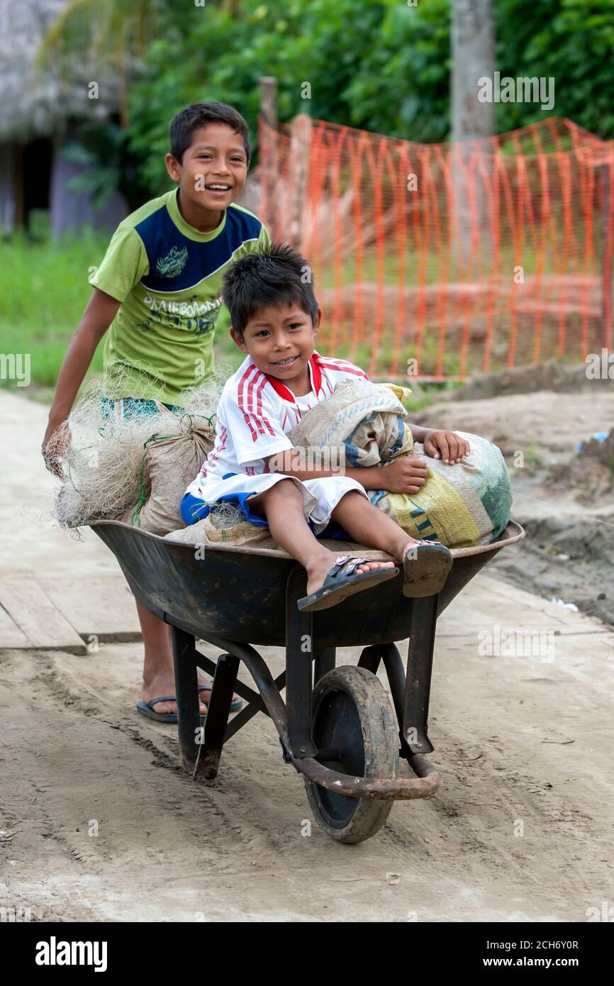 Boys pushing a wheel barrow loaded with sacks along a street in the