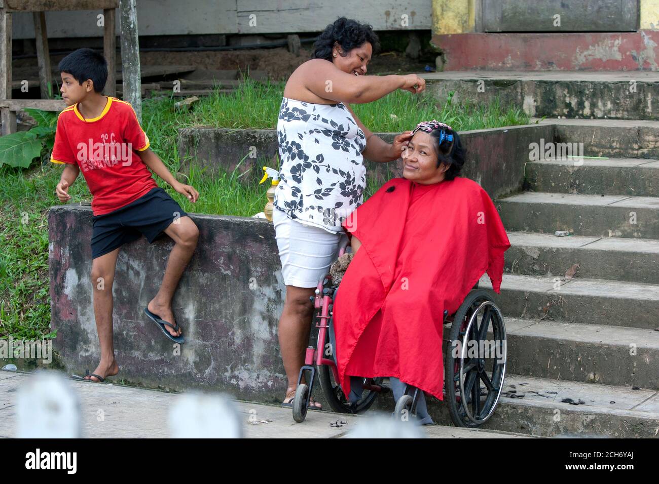 A lady has her hair styled whilst sitting in a wheelchair on the street