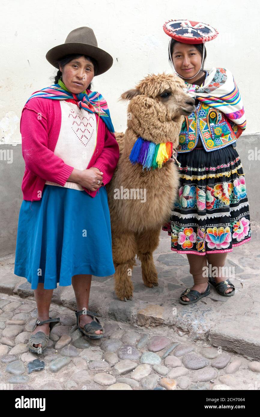 Peruvian ladies dressed in colourful traditional clothes including a poncho  stand with a llama against a wall on a street at Cusco in Peru Stock Photo  - Alamy