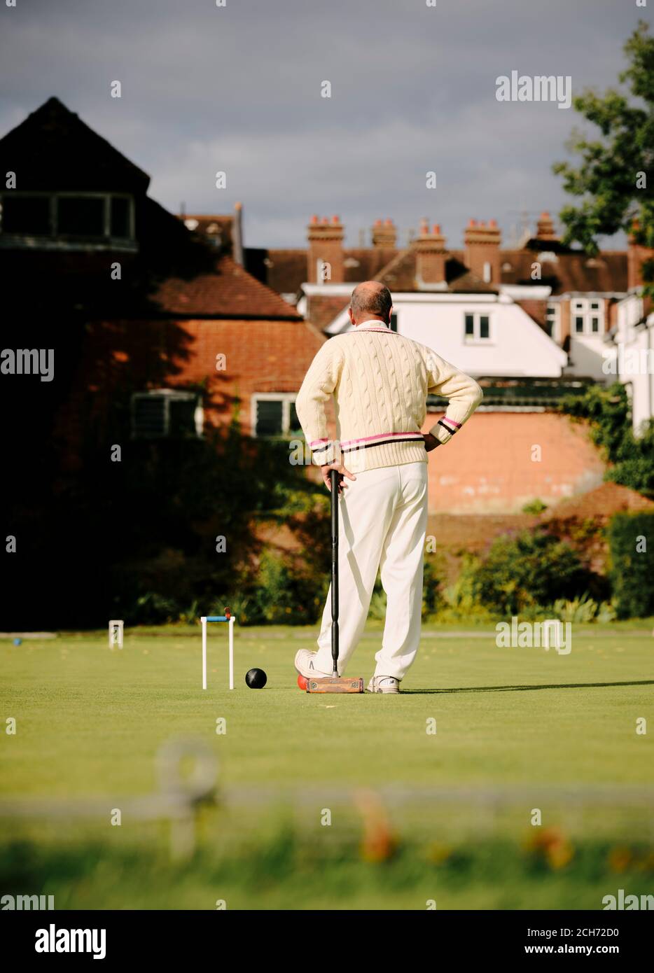 A man dressed in traditional whites playing lawn croquet holding a croquet mallet next to a hoop on a summers day in the UK - summer sport Stock Photo