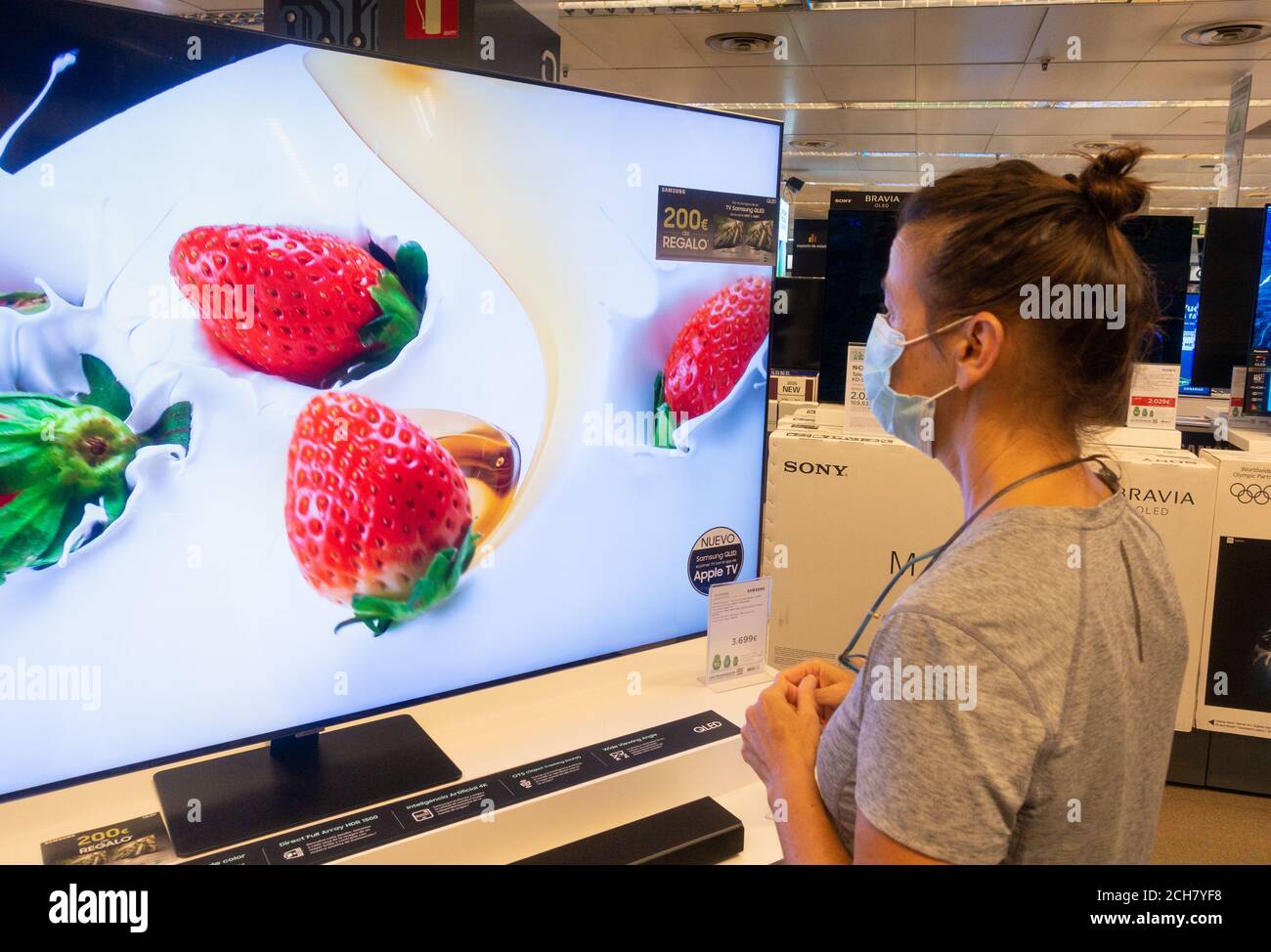 Woman wearing face mask looking at high definition television, TV screen in store. Stock Photo