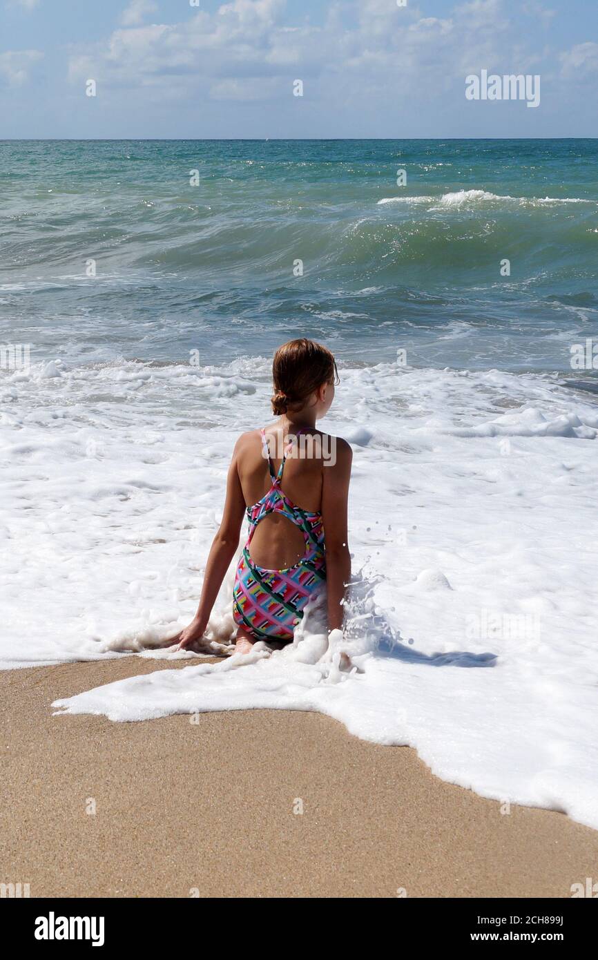 teenage girl sitting in white sea foam and looking at the sea. Stock Photo