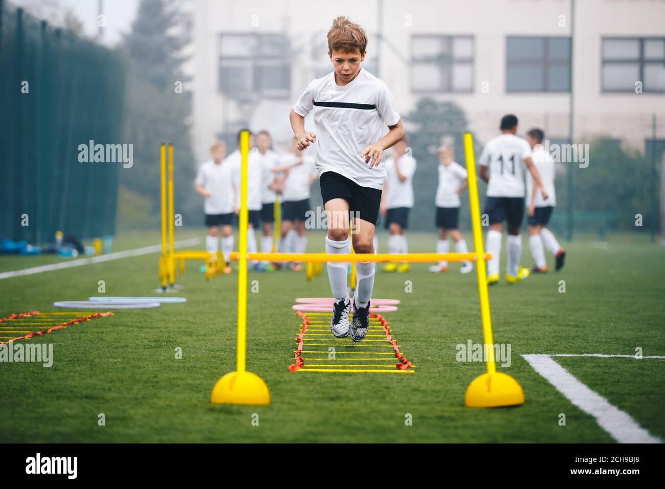 Boys on Agility Training on School Soccer Pitch. Athlete Soccer Player In Training. Young Boy Running Through Ladder and Skipping. Agility Ladder Dril Stock Photo