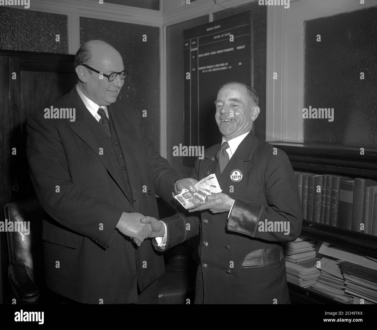 Smiling bus driver holding ten £1 notes is Albert Edward Gunter, who 'jumped the gap' when London's Tower Bridge opened while his bus was crossing it. The reward, presented at London Transport headquarters in Westminster by John B. Burnell, Operating Manager of London Transport's Central Road Services, was a gift from the Board to mark his heroism. Stock Photo