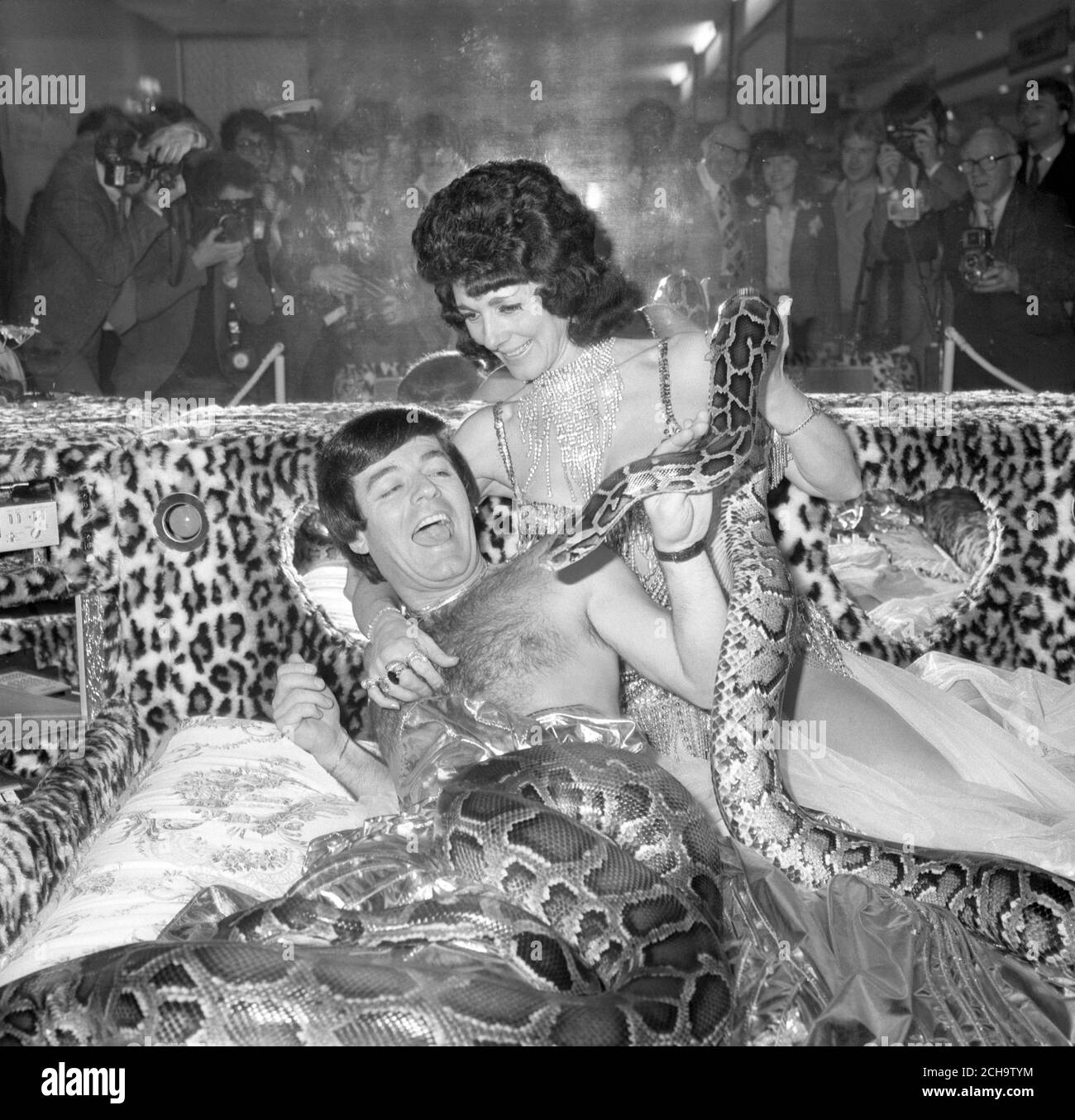 Radio DJ Tony Blackburn is joined by the slithery pets of snake dancer Sheba as he tries out what is claimed to be the most luxurious bed ever built. The 'Queen of Sheba' bed by Valentino is on view at the Daily Mail Ideal Home Exhibition at Earl's Court, London. It features record and cassette decks, a TV, video recorder, a fridge, and a hidden machine that releases exotic perfumes at given intervals. Stock Photo