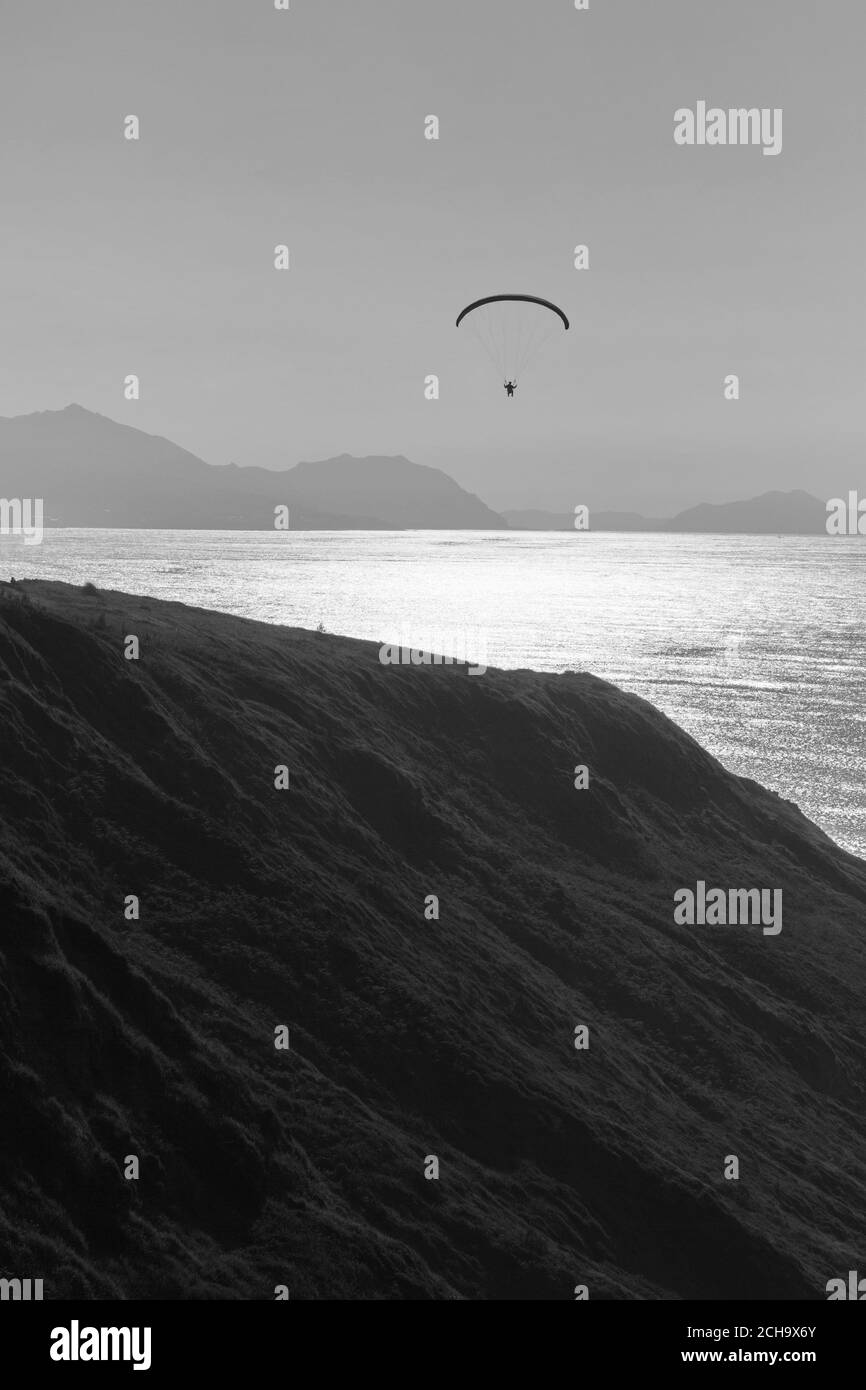 Person practicing paragliding on the cliffs of the coast. Black and white photo. Stock Photo
