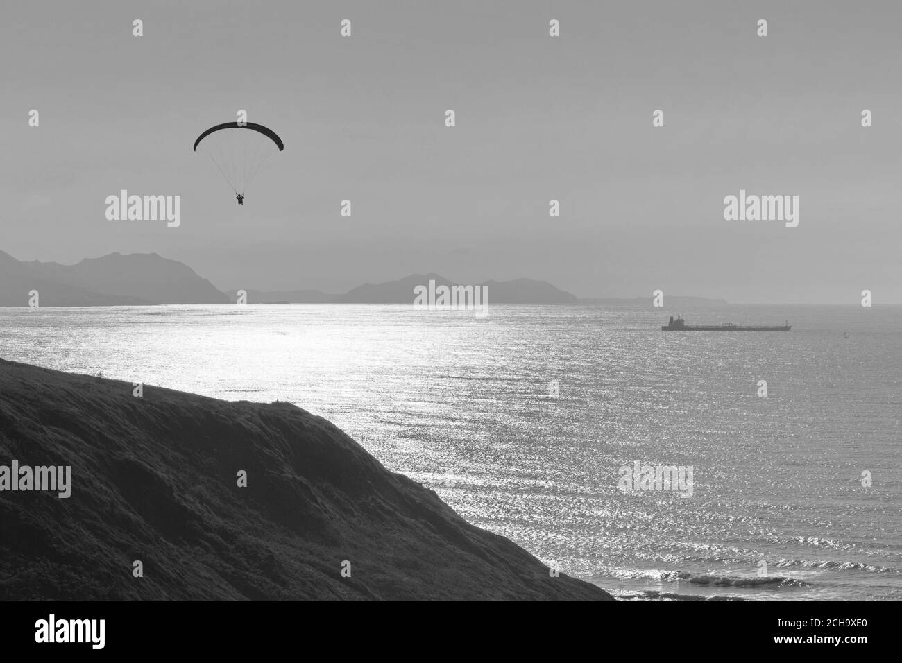 Person practicing paragliding on the cliffs of the coast. Black and white photo. Stock Photo