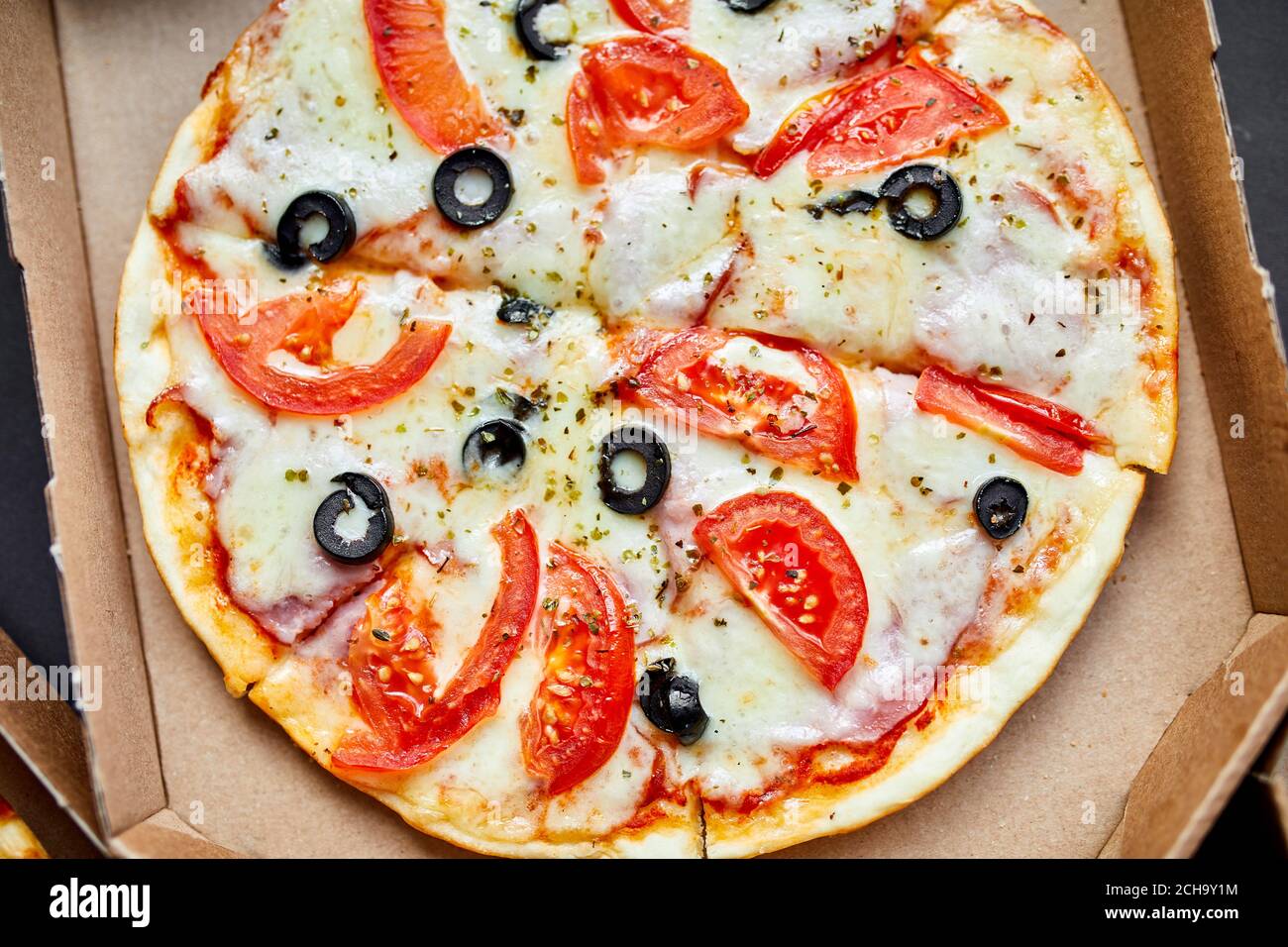 Open box with hot tasty italian sliced pizza on black background Stock