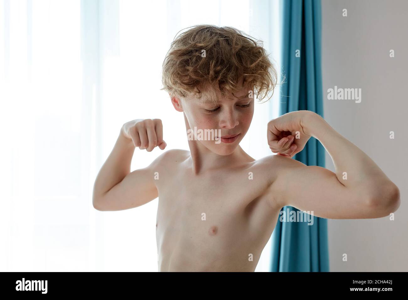 young caucasian teenager boy showing arms muscles, proud. fitness concept. at home Stock Photo
