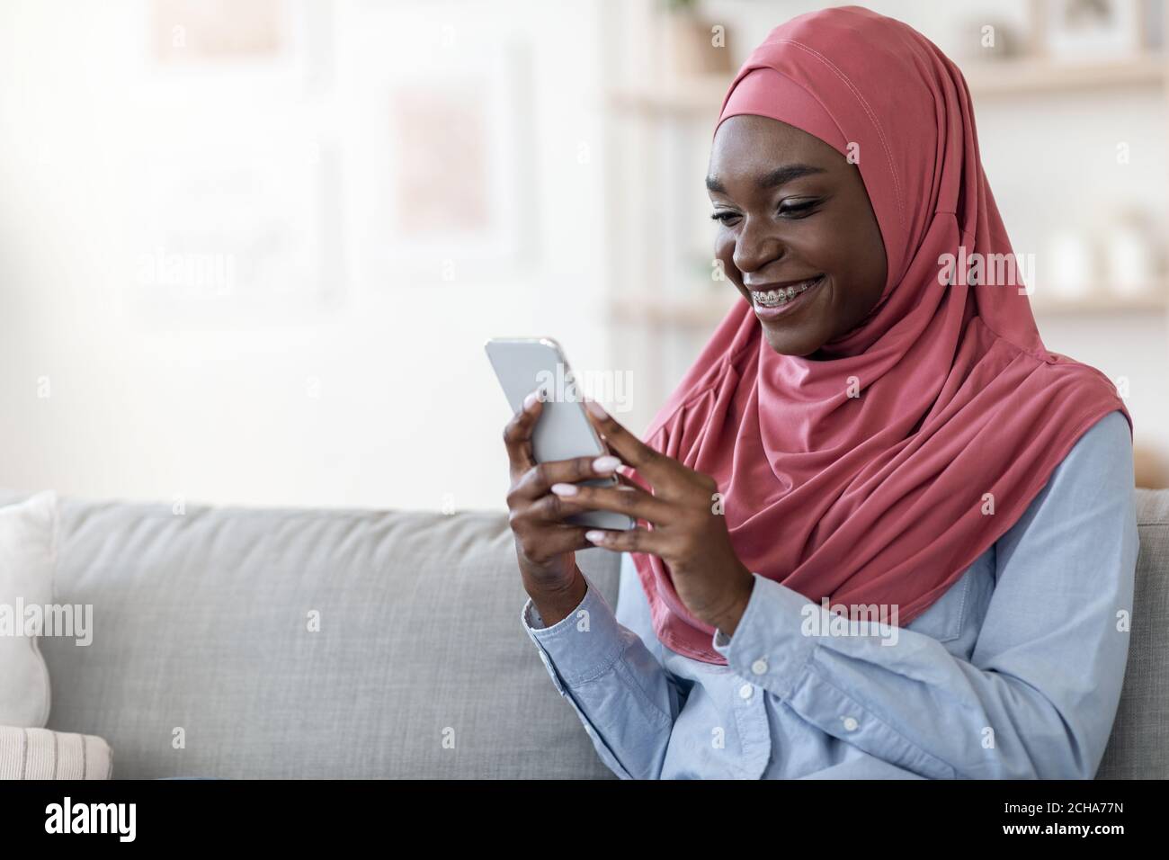 Happy black muslim woman in hijab using smartphone at home Stock Photo ...