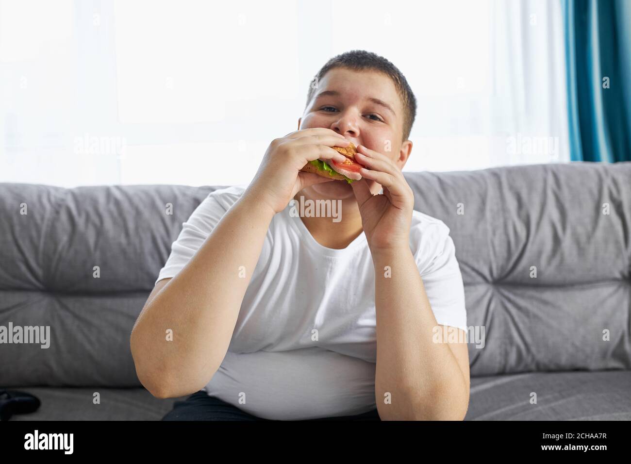 overweight boy lead unhealthy lifestyle, lazy boy watch tv and eat junk food sandwich Stock Photo