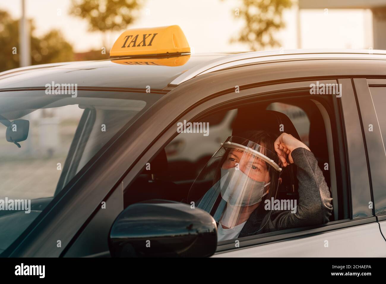 Female taxi driver with protective face mask and plastic visor waiting
