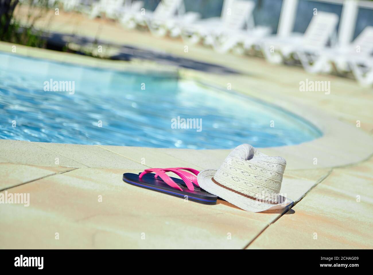 hat and pink flip flops near the swimming pool with blue water, summer ...