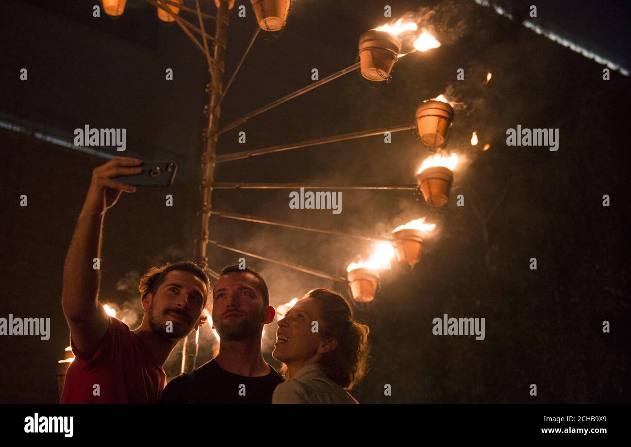 People take a selfie in front of a burning structure as a part of 'Fire Garden' by Compagnie Carabosse, in front of the Tate Modern in London to mark the 350th anniversary of the Great Fire of London. Stock Photo