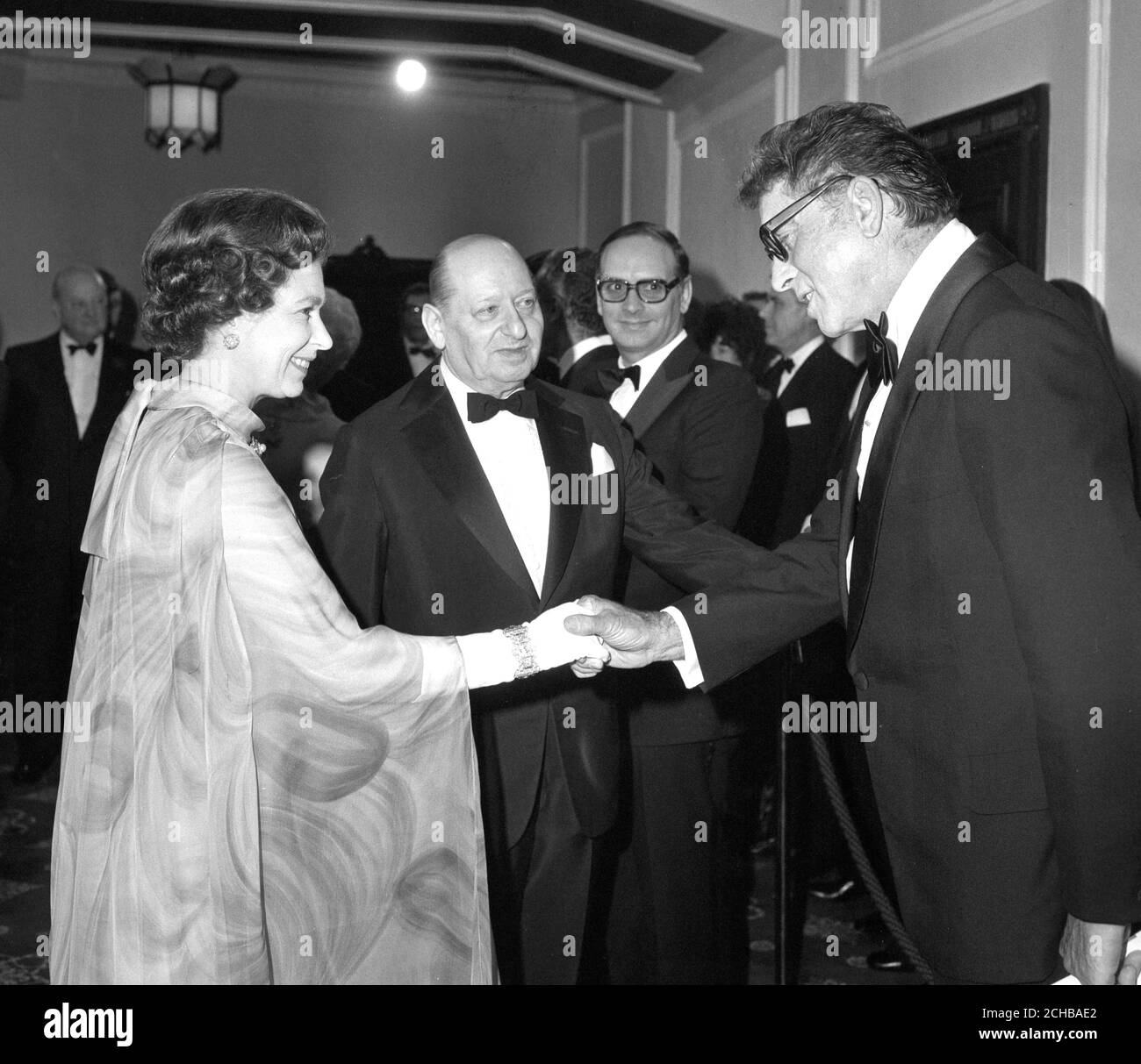 Queen Elizabeth II shakes hands with Hollywood's Burt Lancaster at the Dominion Cinema in London at a Royal premiere of his new film Moses. Looking on is Sir Lew Grade, who presents the film which is released in the UK by Scotia-Barber Distributors. The premiere aids the British Olympics Appeal Fund. Stock Photo