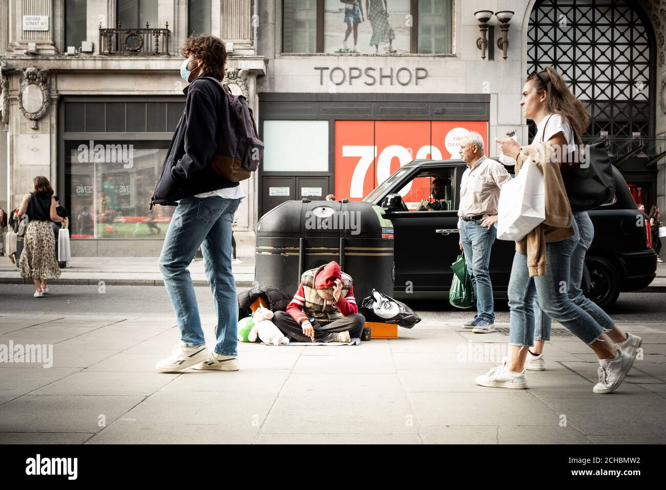 London- September, 2020: A homeless man sits slumped as shoppers walk by on Oxford Street Stock Photo