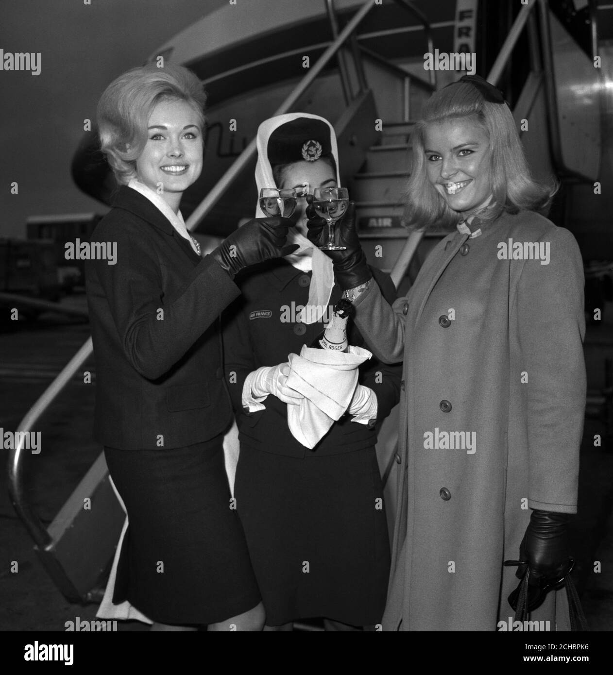 Miss Canada Diane Coulter (l) and Miss France Michele Boule (r), drink a champagne toast as they wish each other good luck in the Miss World contest. They were welcomed on arrival at London Airport by Clare Kaasik (centre), who holds the titles of Miss Air France and Miss London Airport 1966. Stock Photo