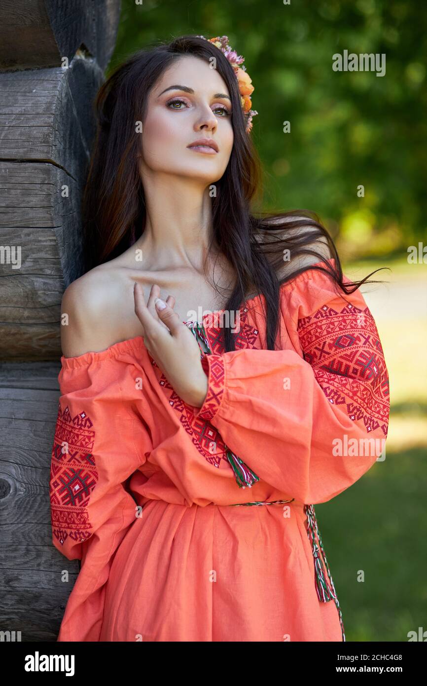 Beautiful Slavic woman in an orange ethnic dress and a wreath of flowers on  her head. Beautiful natural makeup. Portrait of a Russian girl Stock Photo  - Alamy