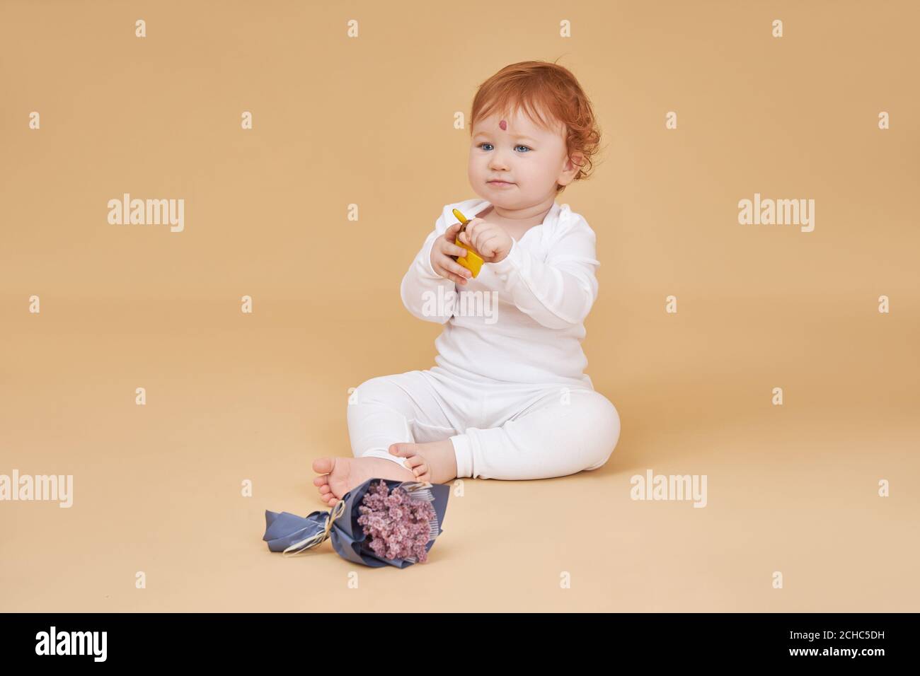 Little red-haired baby girl is playing on a beige background. Big mole on the forehead, not like everyone else Stock Photo