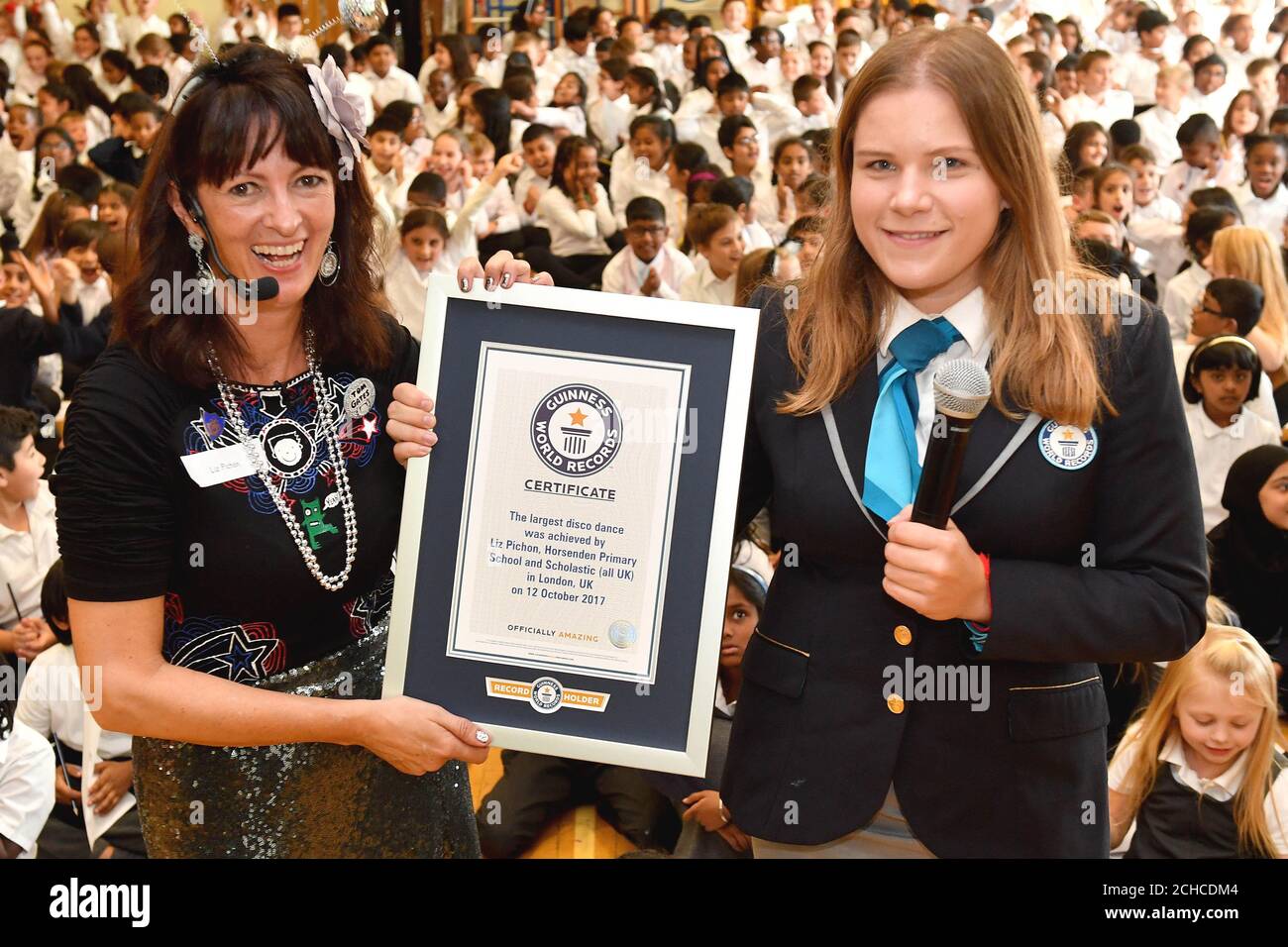 EDITORIAL USE ONLY Author Liz Pichon (left) collects the record from Adjudicator Paulina Sapinska as 314 pupils from Horsenden Primary School in Middlesex break a Guinness World Records title for largest disco dance, which had previously been 280, to celebrate the launch of Liz's new book Tom Gates:Epic Adventure (Kind of!) published by Scholastic UK.  Stock Photo