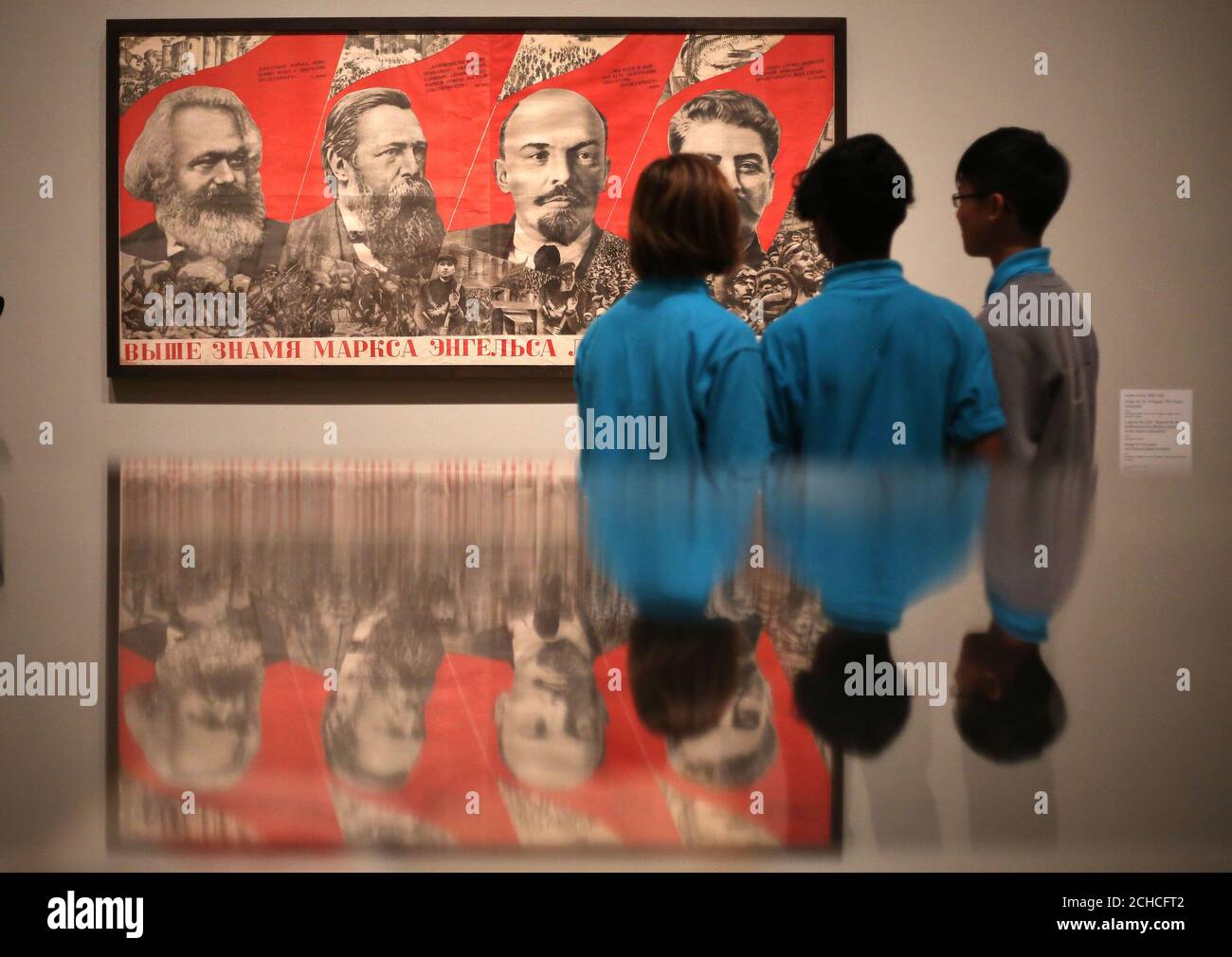 School children from Thomas Tallis School look 'Raise Higher the Banner of Marx, Engels, Lenin and Stalin' a Lithograph on paper by Gustav Klutsis on display at the Red Star Over Russia exhibition at the Tate Modern in London. Stock Photo