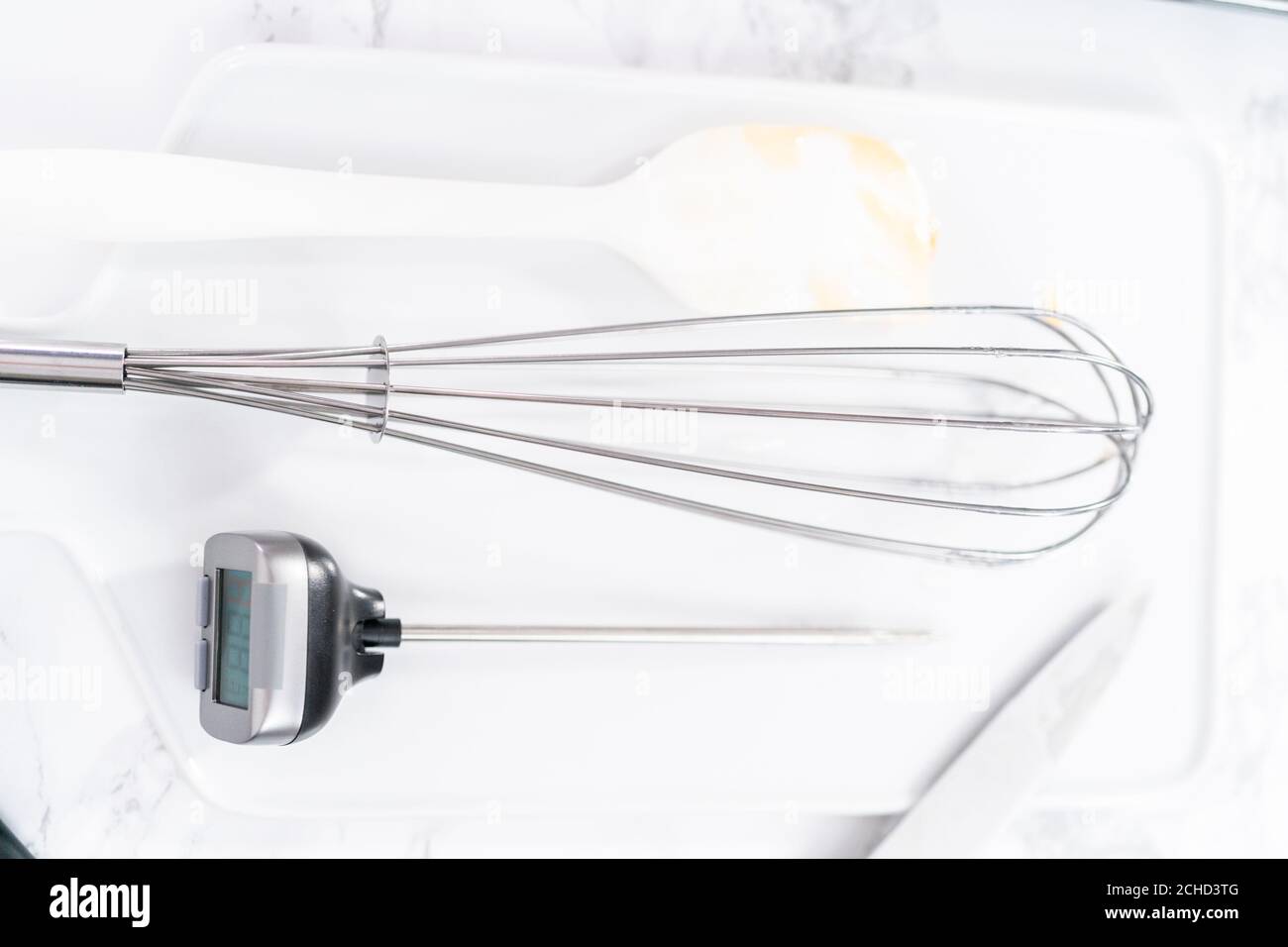 https://c8.alamy.com/comp/2CHD3TG/kitchen-whisk-and-candy-thermometer-on-a-white-cutting-board-2CHD3TG.jpg