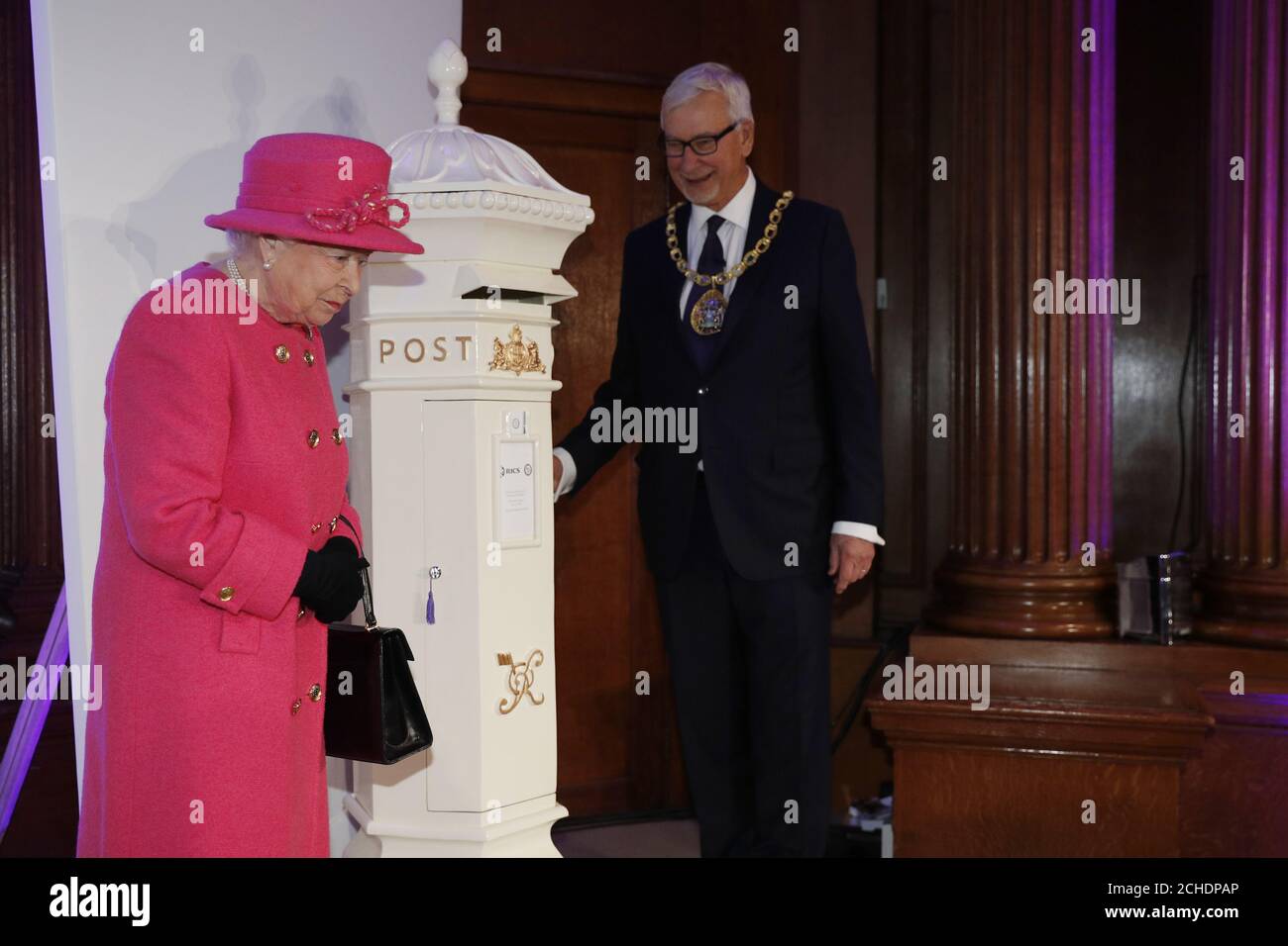RICS President John Hughes watches as Queen Elizabeth II locks a time capsule in the form of a post box, during a visit to the Royal Institution of Chartered Surveyors (RICS) in London, to mark its 150th anniversary. Stock Photo