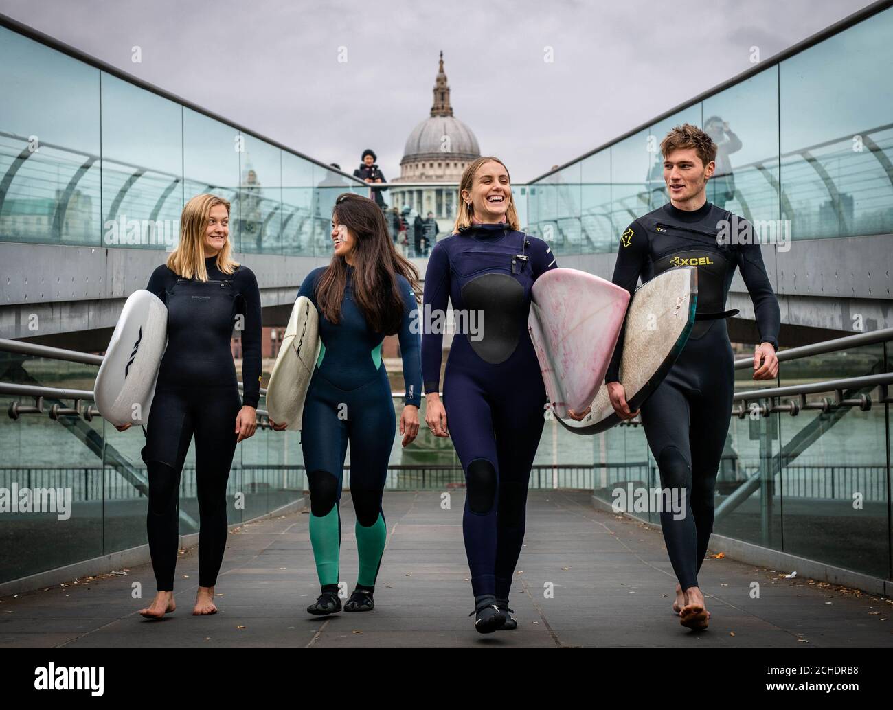 (Left to right) Surfers Jessica Rowe, Veranika Lim, Sophie Hellyer and Frank Hodgson cross London's Millennium Bridge as a partnership is announced between Lee Valley Regional Park Authority and The Wave to create an inland surfing destination in the capital for people of all ages, backgrounds and abilities. Stock Photo