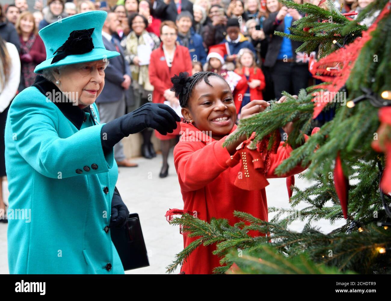 Queen Elizabeth II and Shylah Gordon, aged 8, attach a bauble to a Christmas tree during her visit to Coram, the UK's oldest children's charity, to open the Queen Elizabeth II Centre at its base in central London. Stock Photo