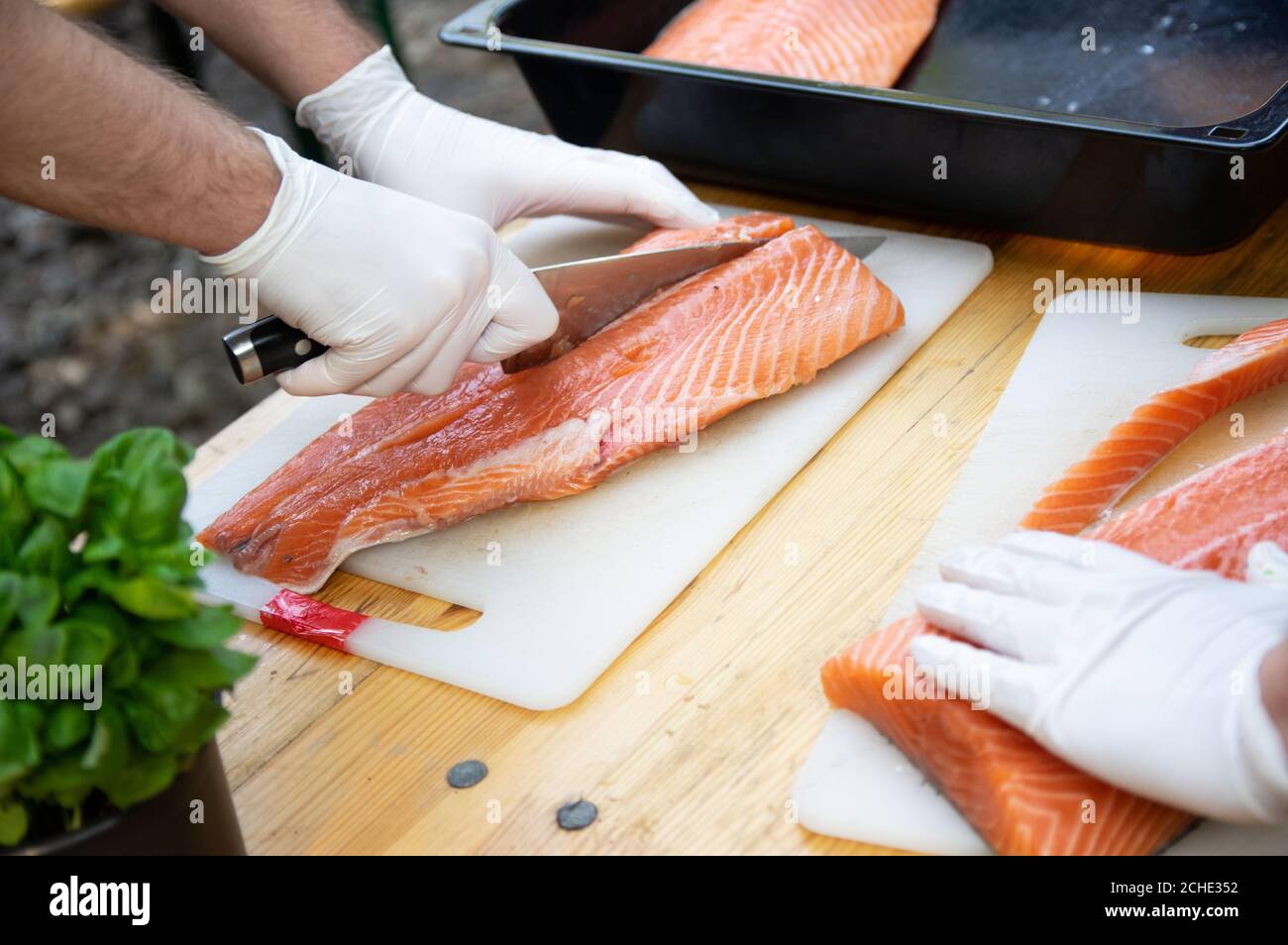 Man hands cutting pink raw salmon with knife on white board Stock Photo