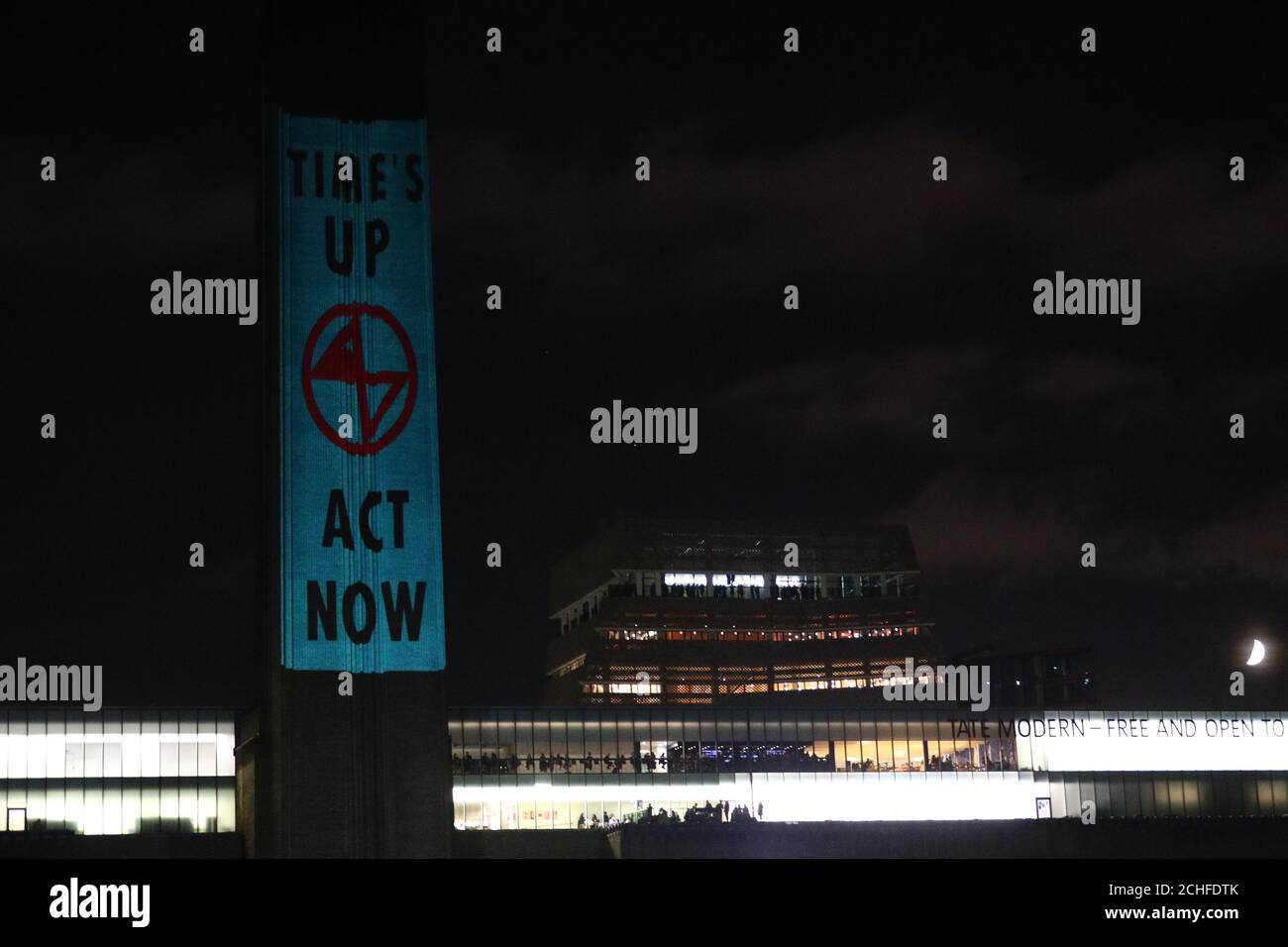 Extinction Rebellion activists walk around the Tate Modern as others project messages onto the building in London. The group announced this week that they will take to the streets in the next fortnight, planning to shut down roads around Westminster and staging a sit-in at City Airport in London as part of their protests. Stock Photo