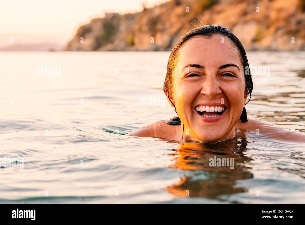 Caucasian woman laughing and showing her white teeth while swimming in sea at sunset Stock Photo