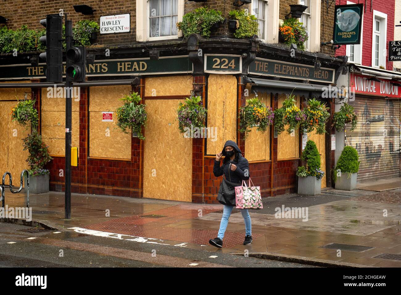 A woman walks past a boarded up pub in north London, as the UK continues in lockdown to help curb the spread of the coronavirus. Stock Photo