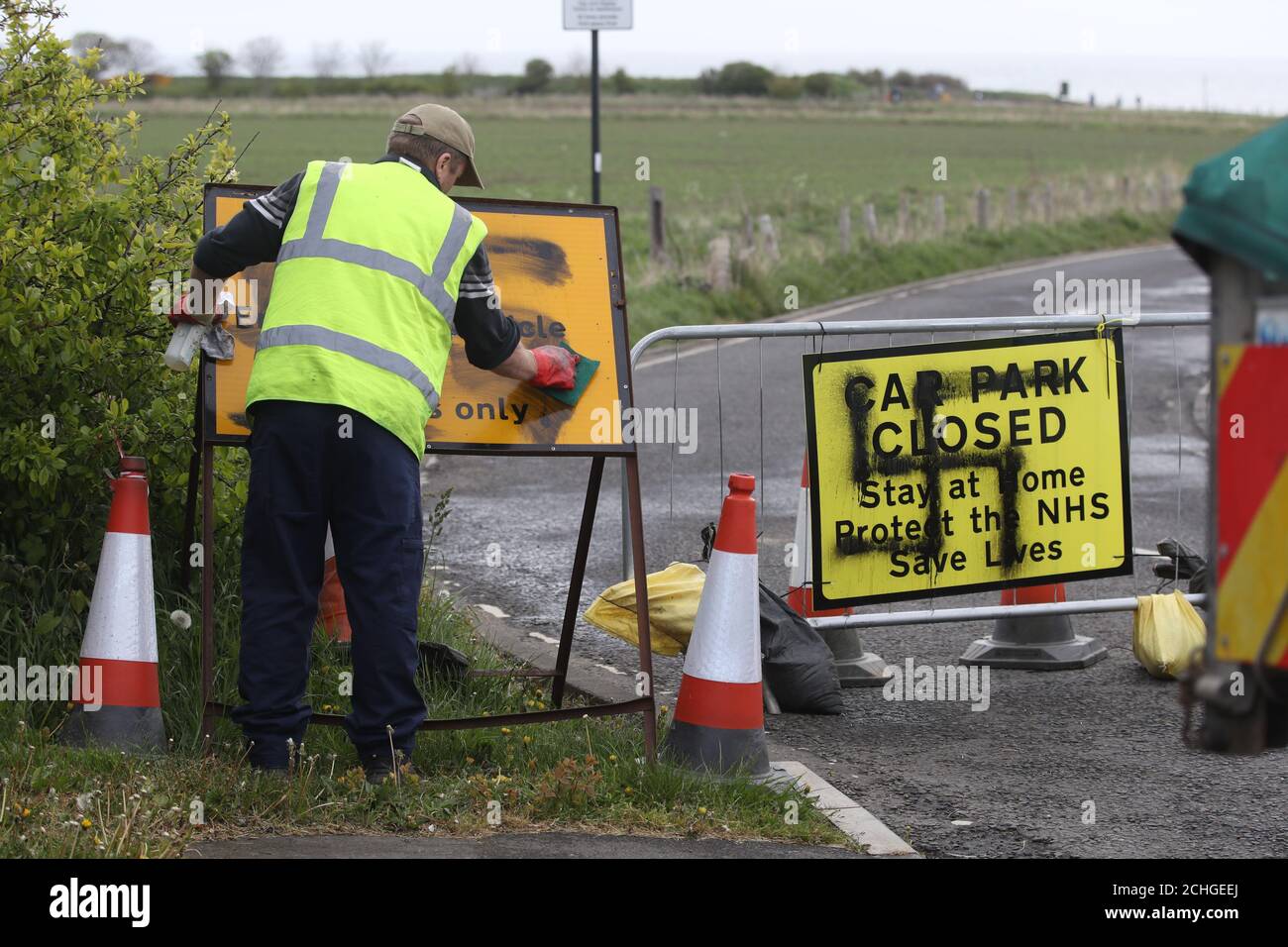 A worker removes a swastika spray painted on a sign at the entrance to a closed road and car park near Whitley Bay lighthouse, Northumberland. Graffiti has appeared on signs at several car parks along the Northumberland coastal road as the UK continues in lockdown to help curb the spread of the coronavirus. Stock Photo