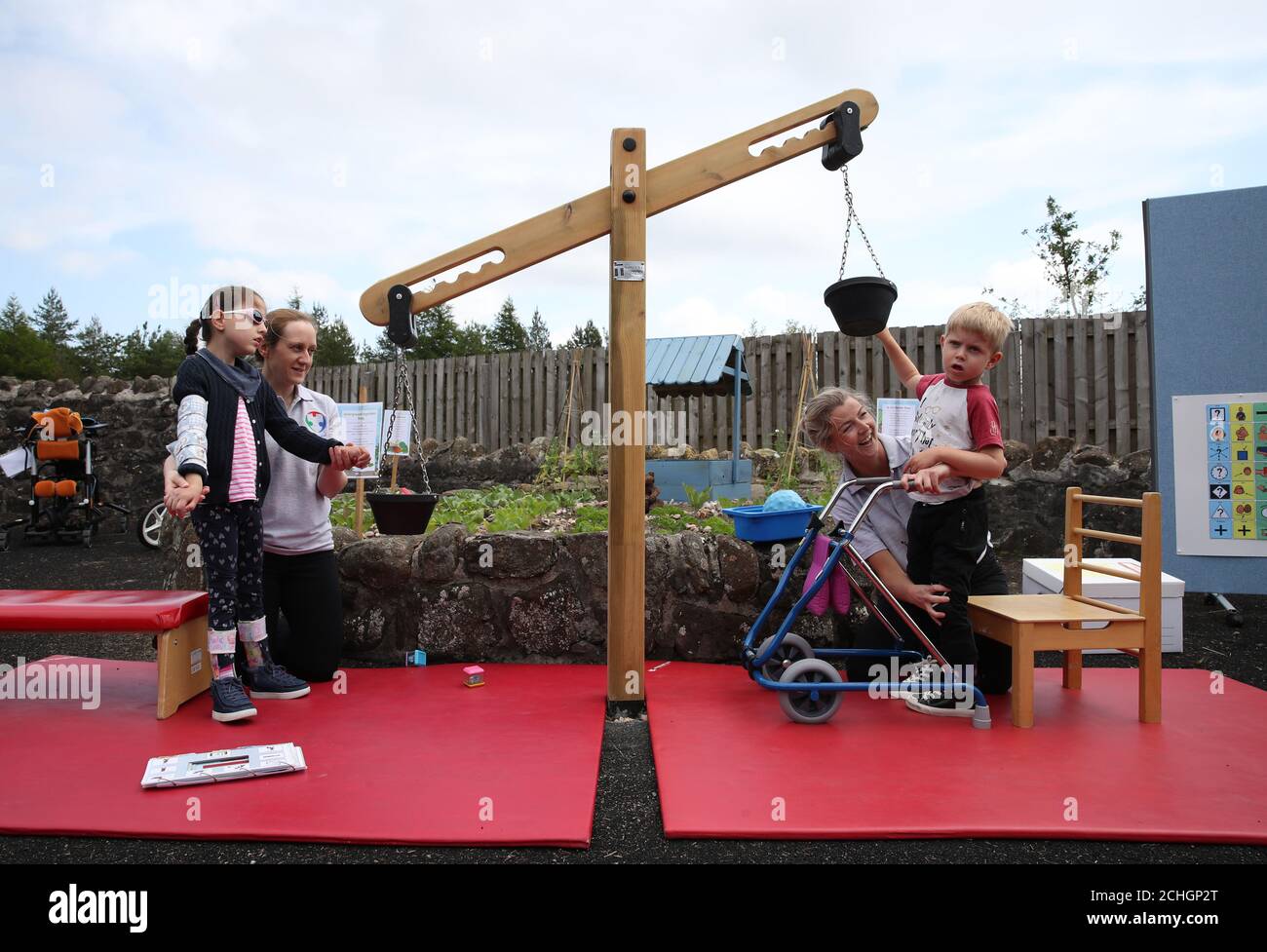Embargoed to 0001 Monday June 22 (left to right) Kim McMaster alongside Specialist Physiotherapist Jenni Coulter and Oliver Cunningham with Specialist Physiotherapist Leah Honohan using the weighing scales during a shared theraplay session in the outside therapy area at the Craighalbert Centre. These sessions are taking place to deliver blended learning to children who are shielding. Coronavirus adaptations have been installed at the Scottish Centre for Children with Motor Impairments, Craighalbert Centre, Cumbernauld, as Scotland continues gradually lifting coronavirus lockdown measures. Stock Photo