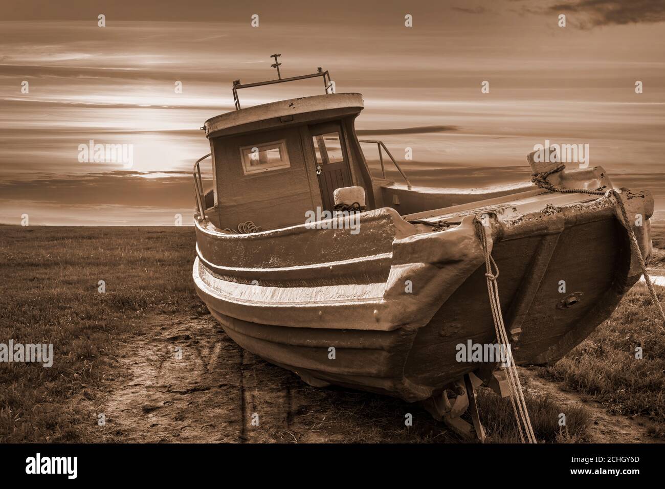 sepia toned old fishing boat lit by sunset at low tide in estuary Stock Photo