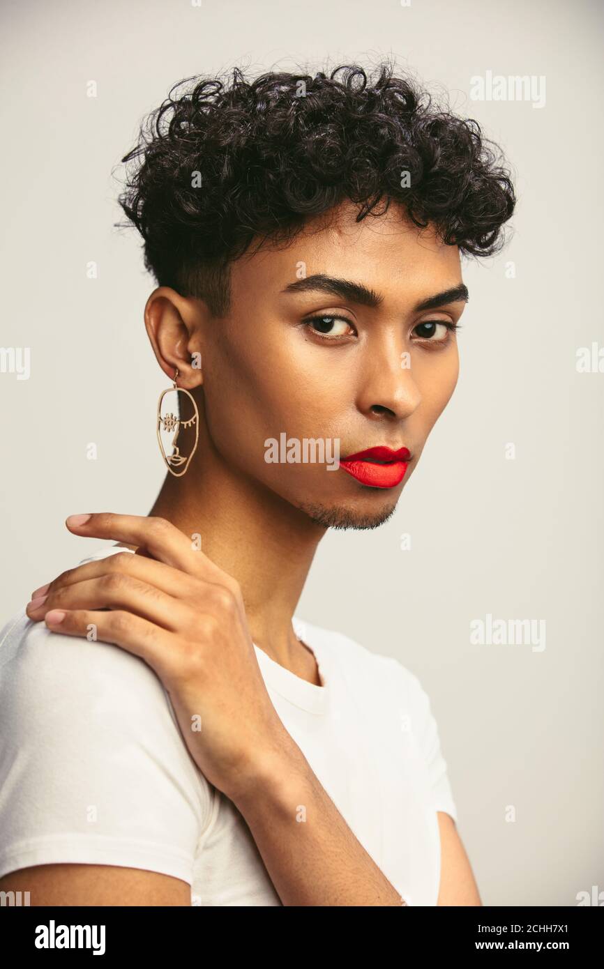 Portrait of a gender fluid gay man wearing earring and red lip stick. Transgender male staring at camera. Stock Photo