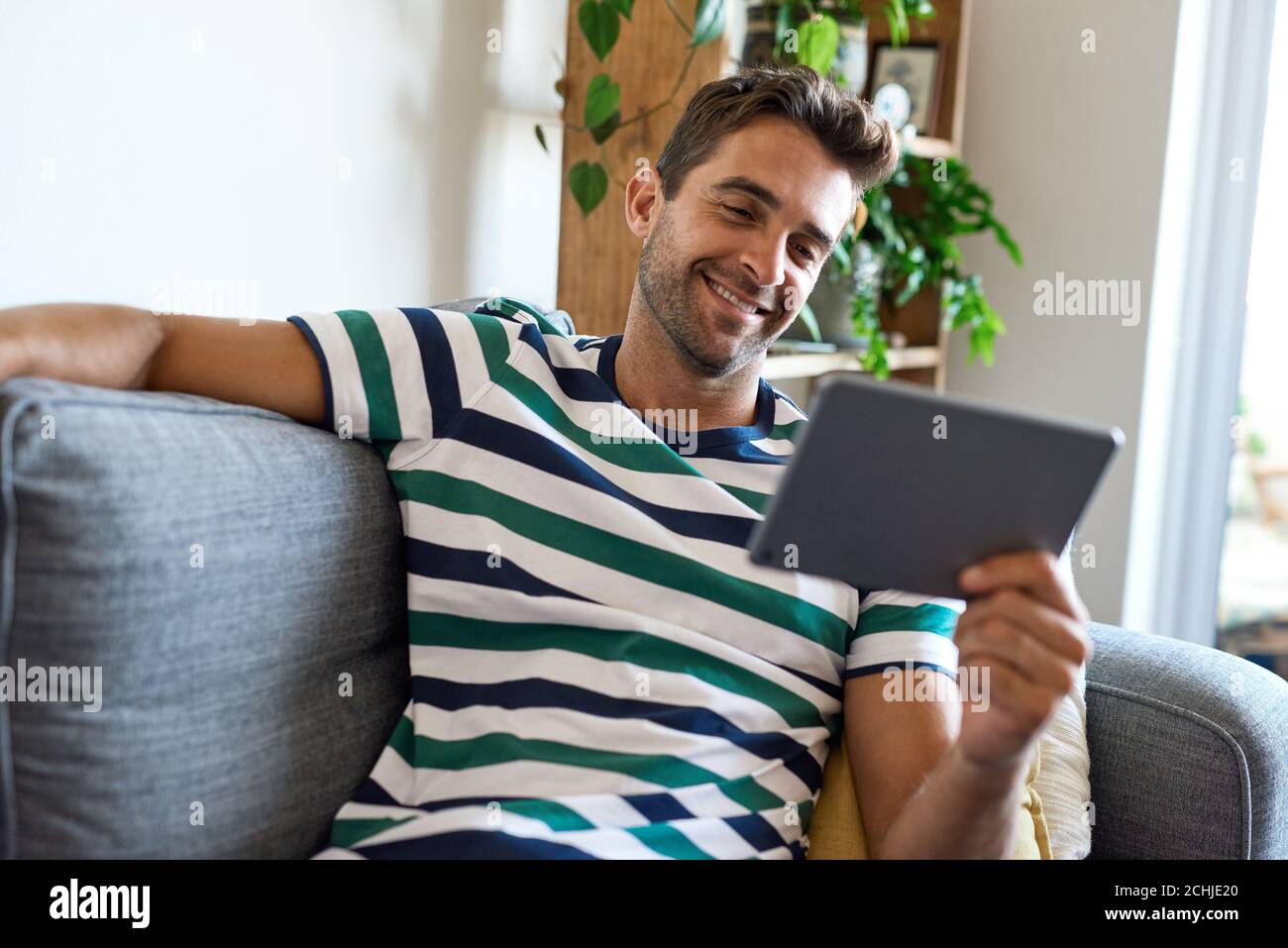Smiling young man sitting at home using a digital tablet Stock Photo