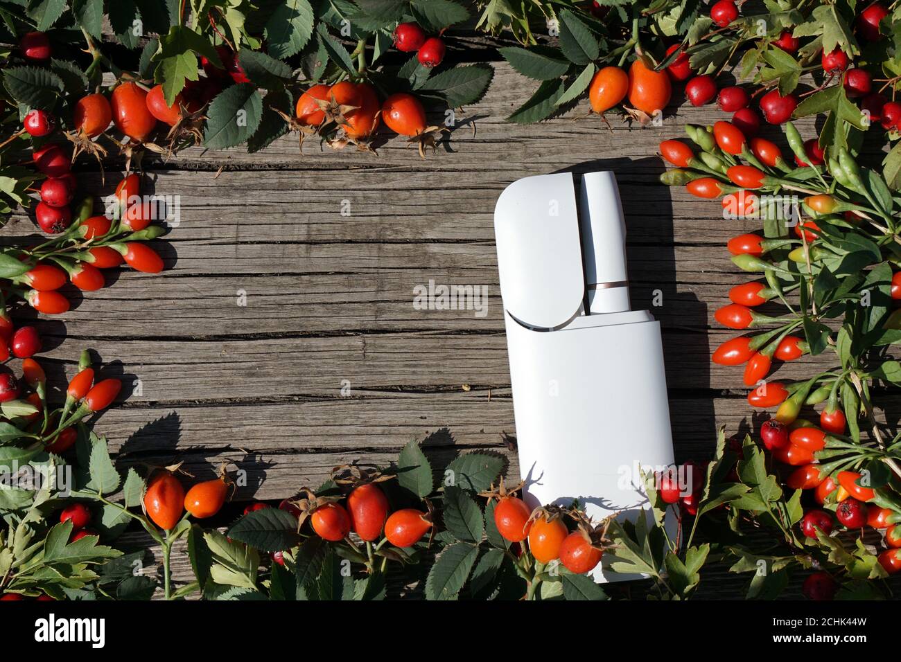 White  battery lies on decorative abstract wooden texture with red berry . This is  new device about  new kind of  technology electronic cigarette Stock Photo