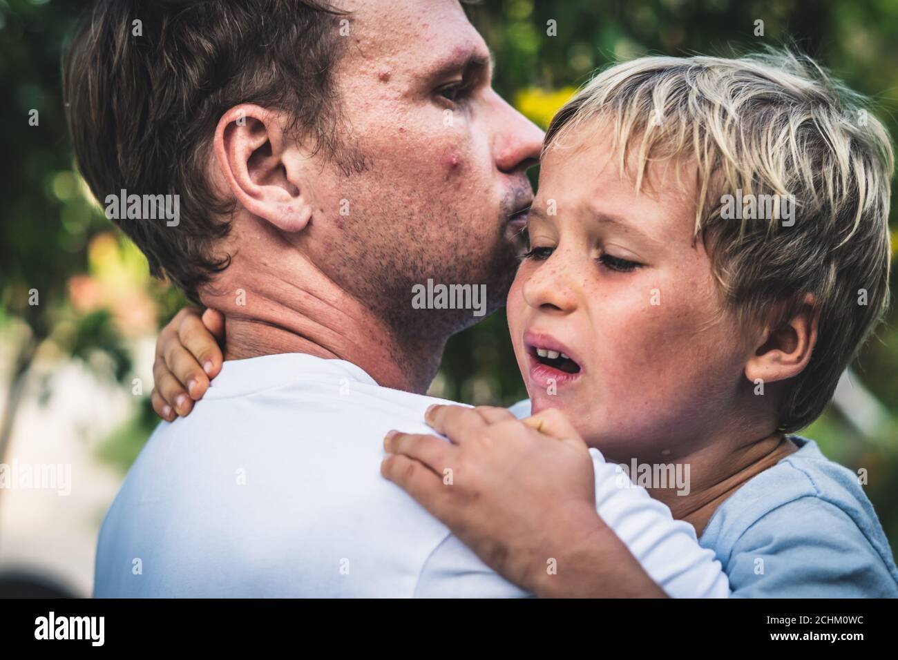 Closeup Sad young blond boy crying on father hands in nature park outdoor. Man holds son, hugs and comforts. Family love, care and moral support, baby Stock Photo