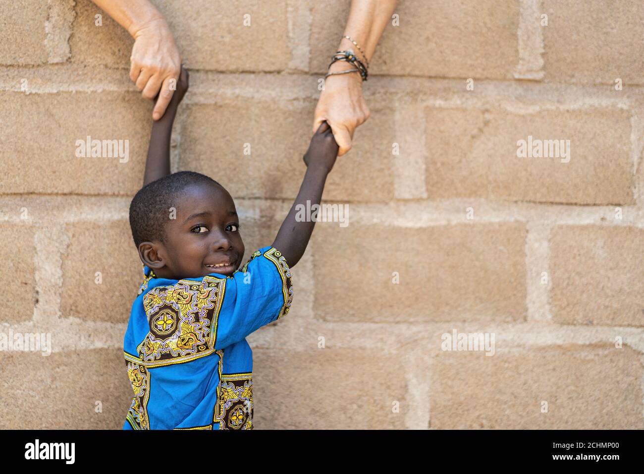 Smiling African Black Boy Gets Help from White Caucasian Woman in front of Wall Stock Photo