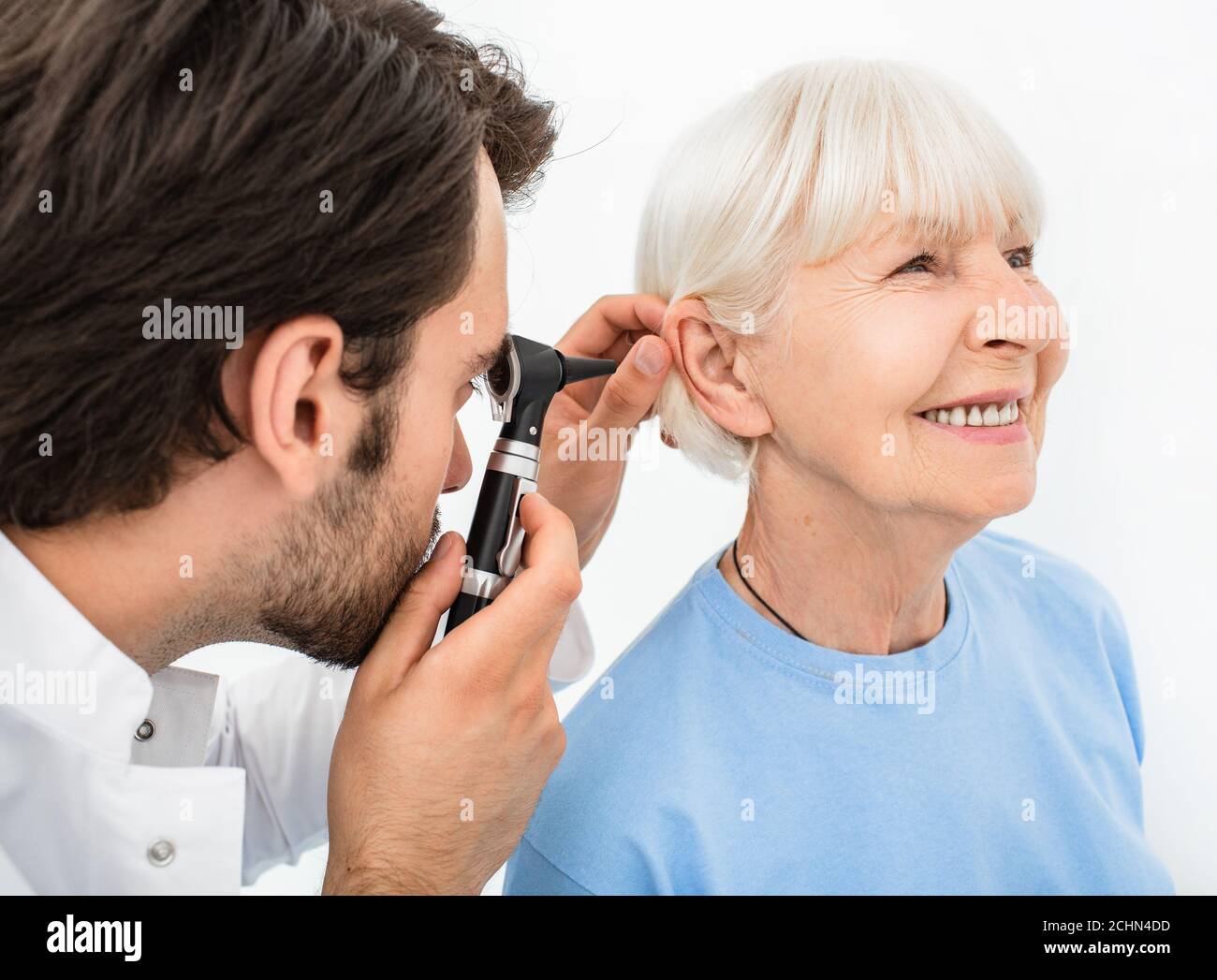 ENT doctor examining senior patient ear, using an otoscope, in doctors office. Elderly smiling woman getting medical ear exam at clinic Stock Photo