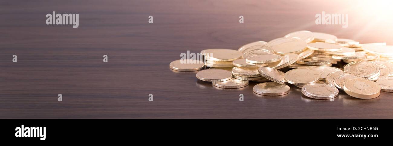 Gold coins scattered on wooden table with light shining Stock Photo