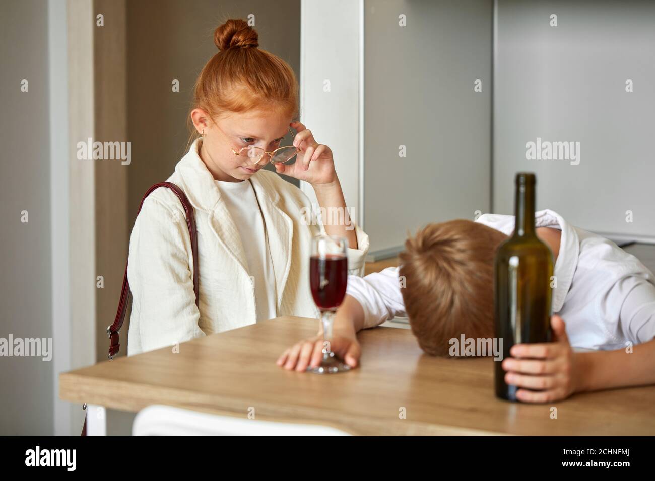 young little caucasian kids couple at home, boy is drinking alcohol, tired of work, get some relax at home. in the kitchen, with redhead girl came fro Stock Photo