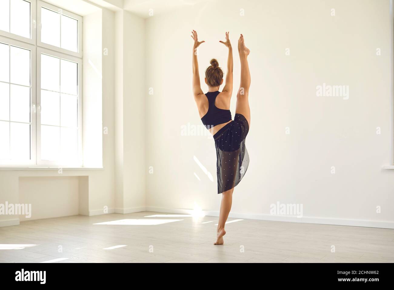 Fit woman in dancewear training her body and practicing standing side split in gym Stock Photo