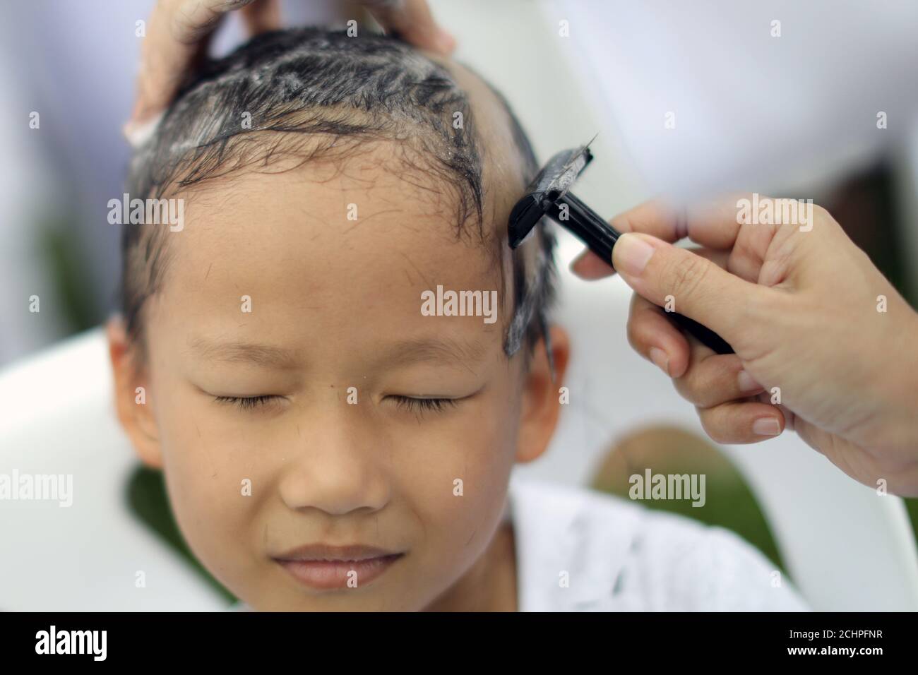 A devotee girl has her hair shaved by her father during a mass novice nun  ordination ceremony to mark the first anniversary of late Thailand's King  Bhumibol Adulyadej's death, at the Sathira-Dhammasathan